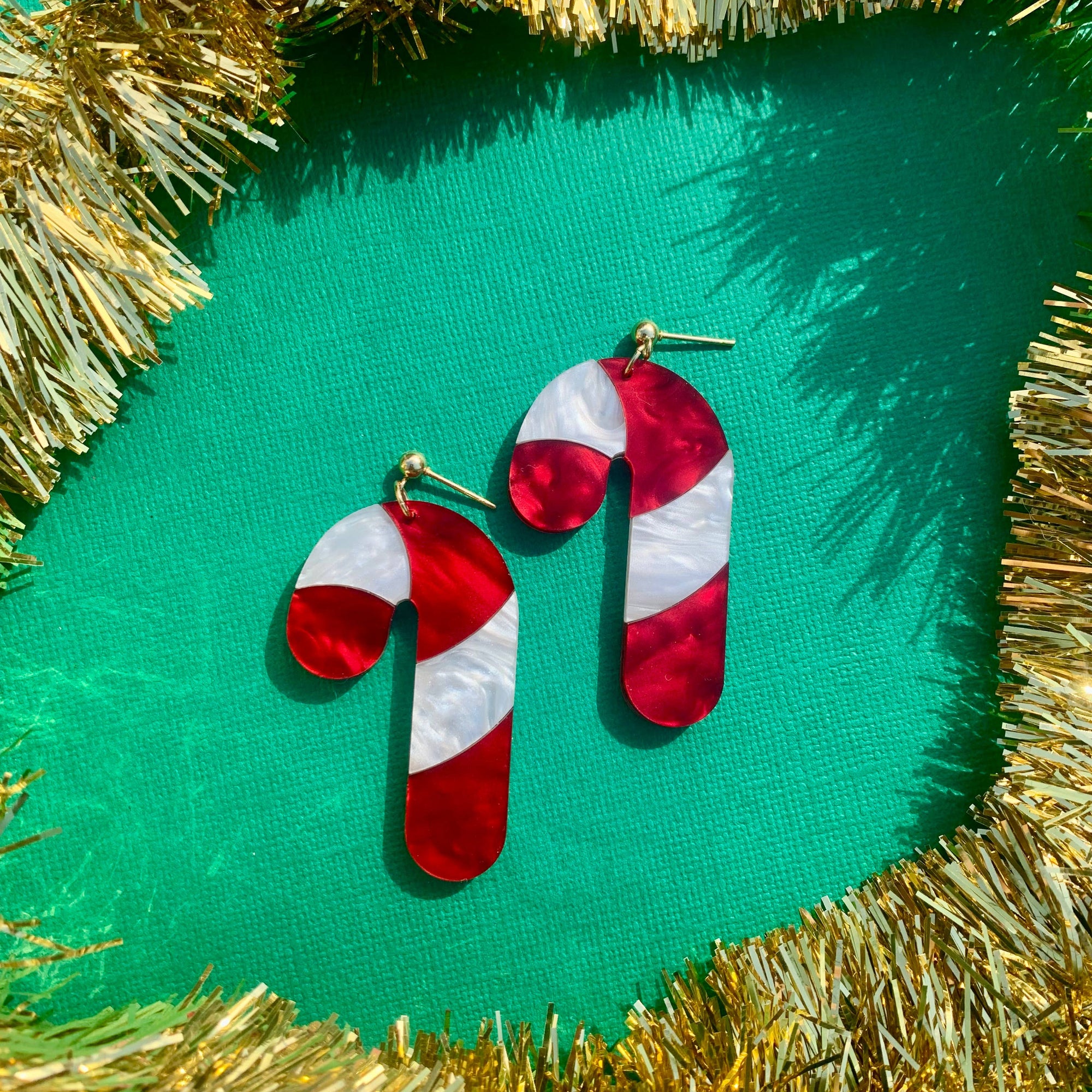 Red and white candy cane-shaped earrings on a green background with gold tinsel