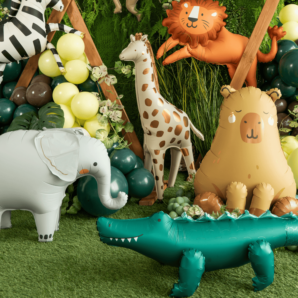 Inflatable animal toys including a lion, giraffe, elephant, and alligator on a grassy surface with balloons and plants.