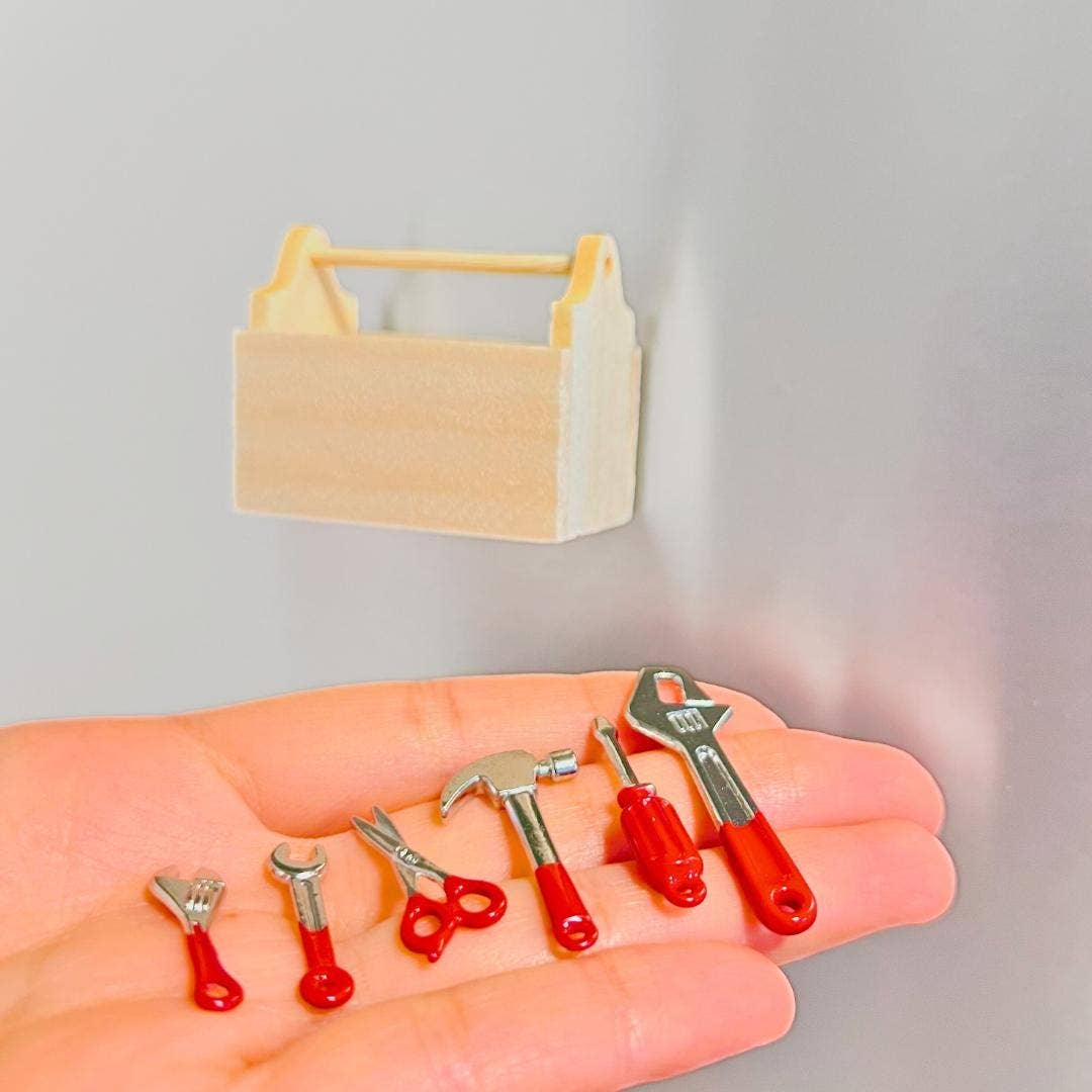 Miniature tools with red handles on a hand, next to a small wooden toolbox on a gray background