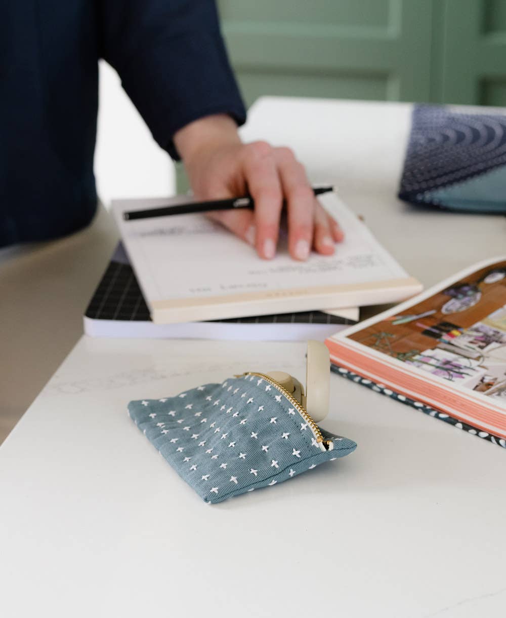 Small blue pouch with gold zipper on a desk with books and a pen