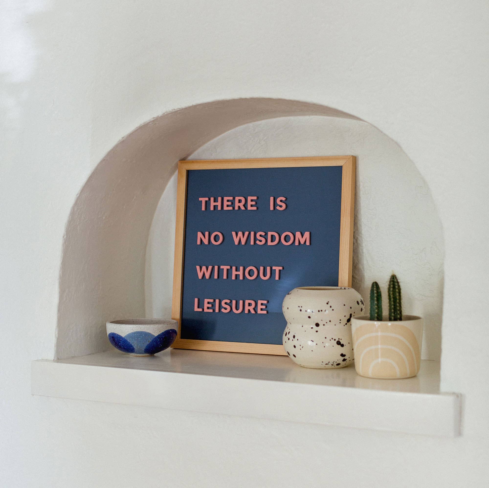 Decorative shelf with a framed quote, ceramic bowl, and small plants against a white wall.