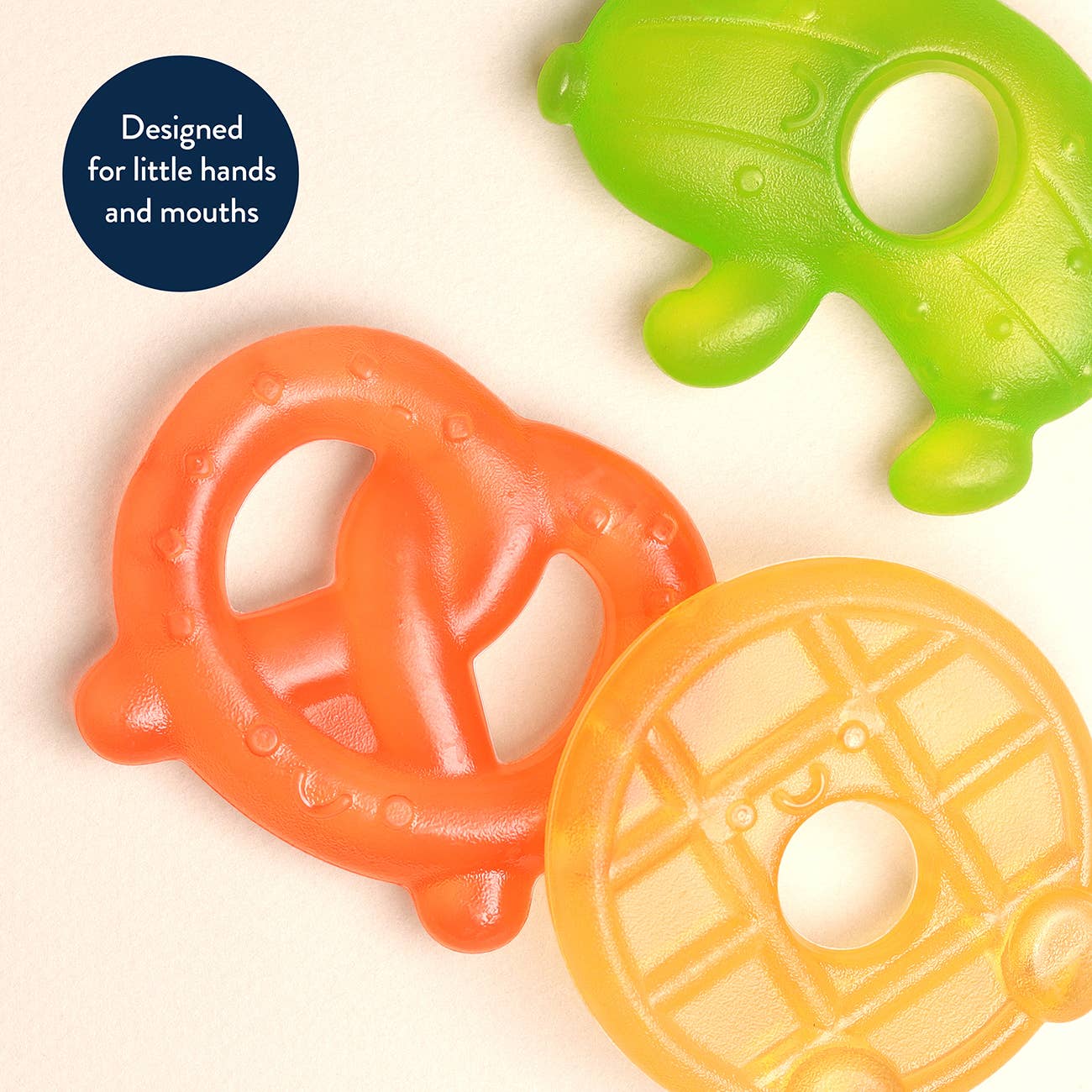 Three colorful silicone teethers shaped like a pretzel, waffle, and turtle on a beige background.