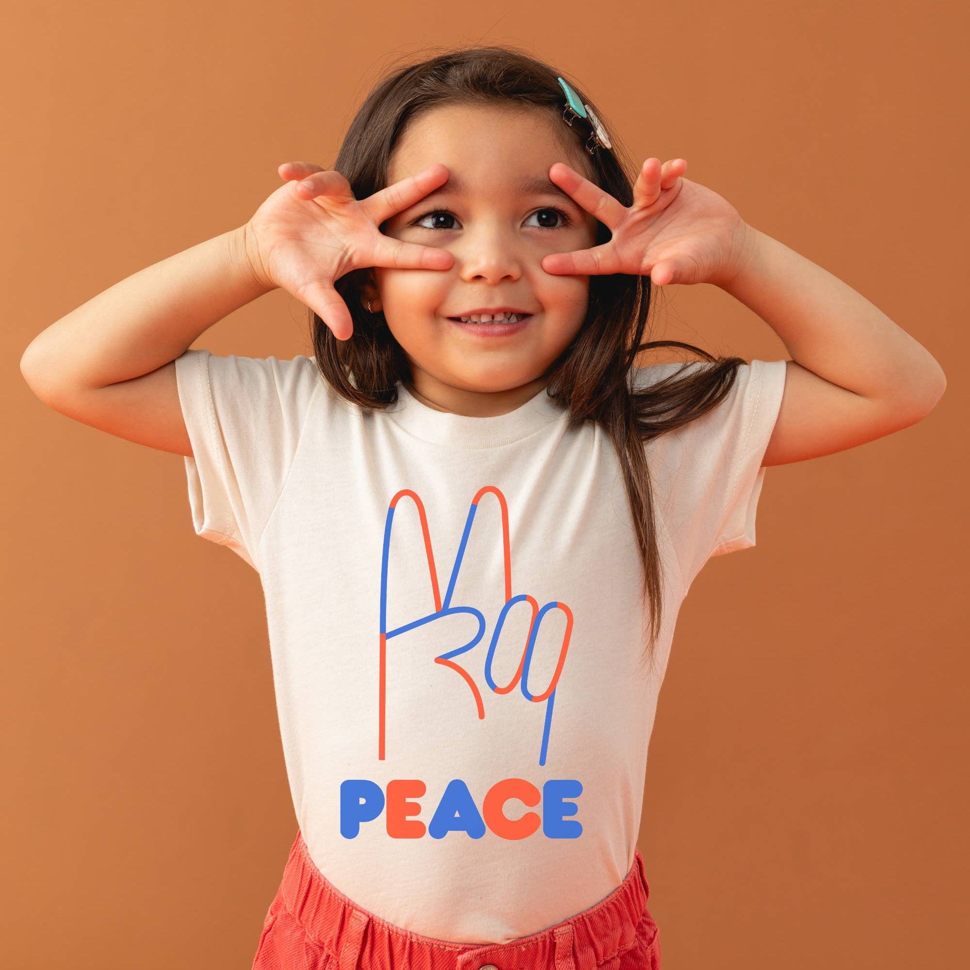 Child wearing a white t-shirt with colorful text and red pants against an orange background