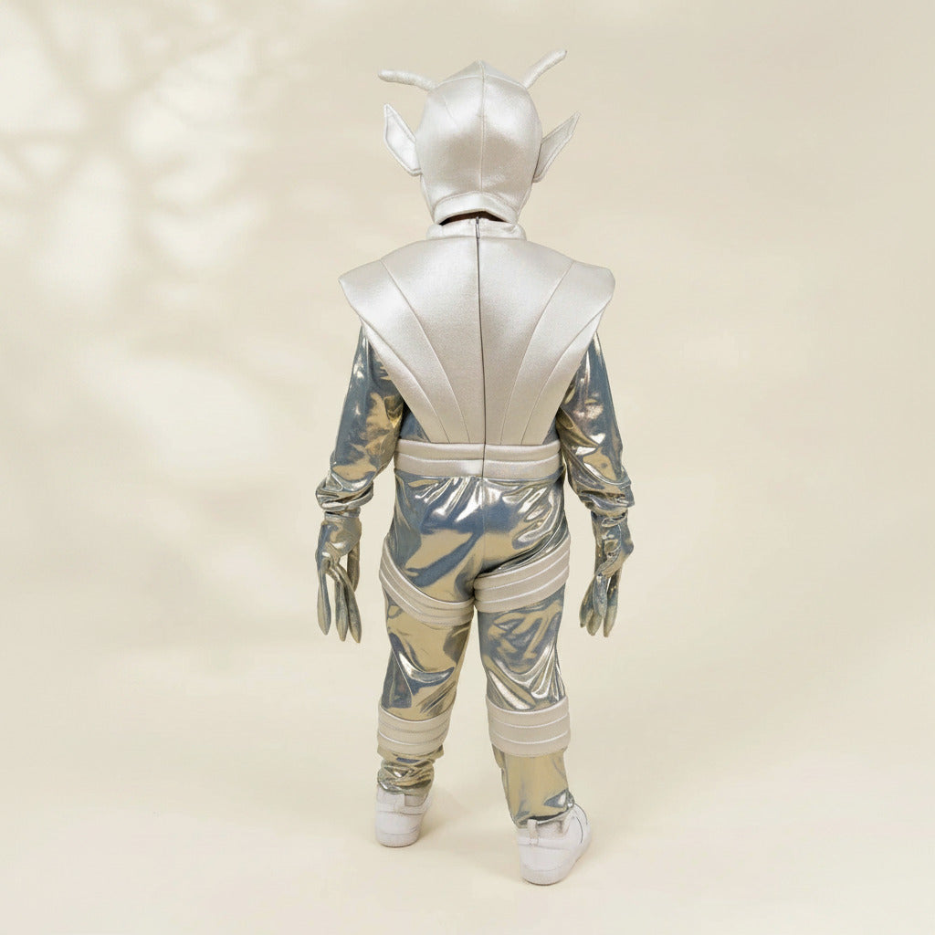 A child wearing a shiny metallic silver alien costume, shown from the back against a light beige studio background.