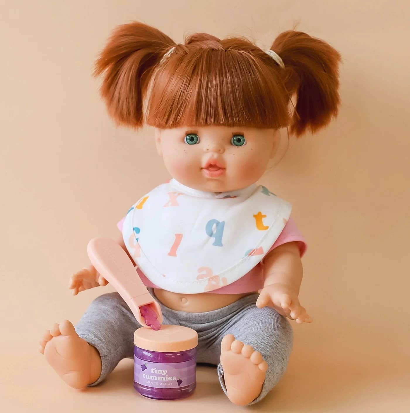 Baby doll with a bib and gray pants holding a purple jar on a beige background