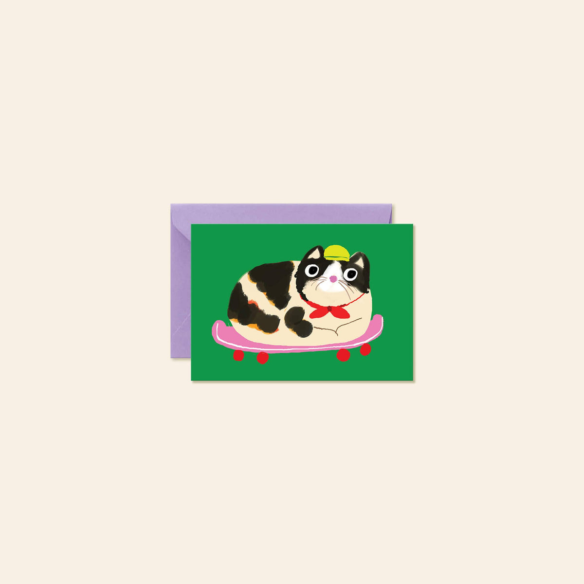 A greeting card featuring a cartoon black-and-white cat wearing a yellow hat and red bow tie while lying on a pink skateboard, shown with a lavender envelope on a light beige background.
