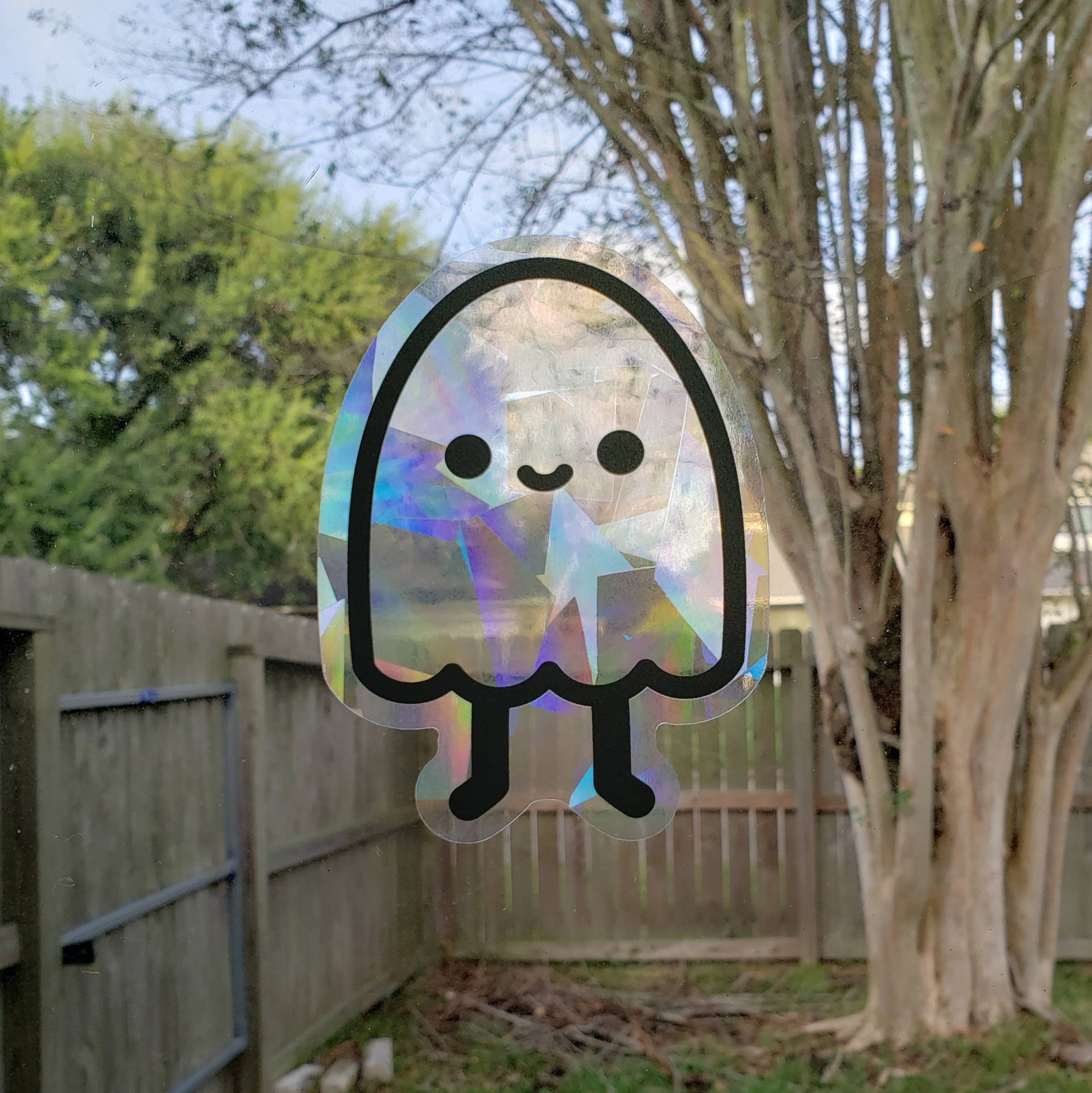 Holographic ghost sticker on a window with a backyard background
