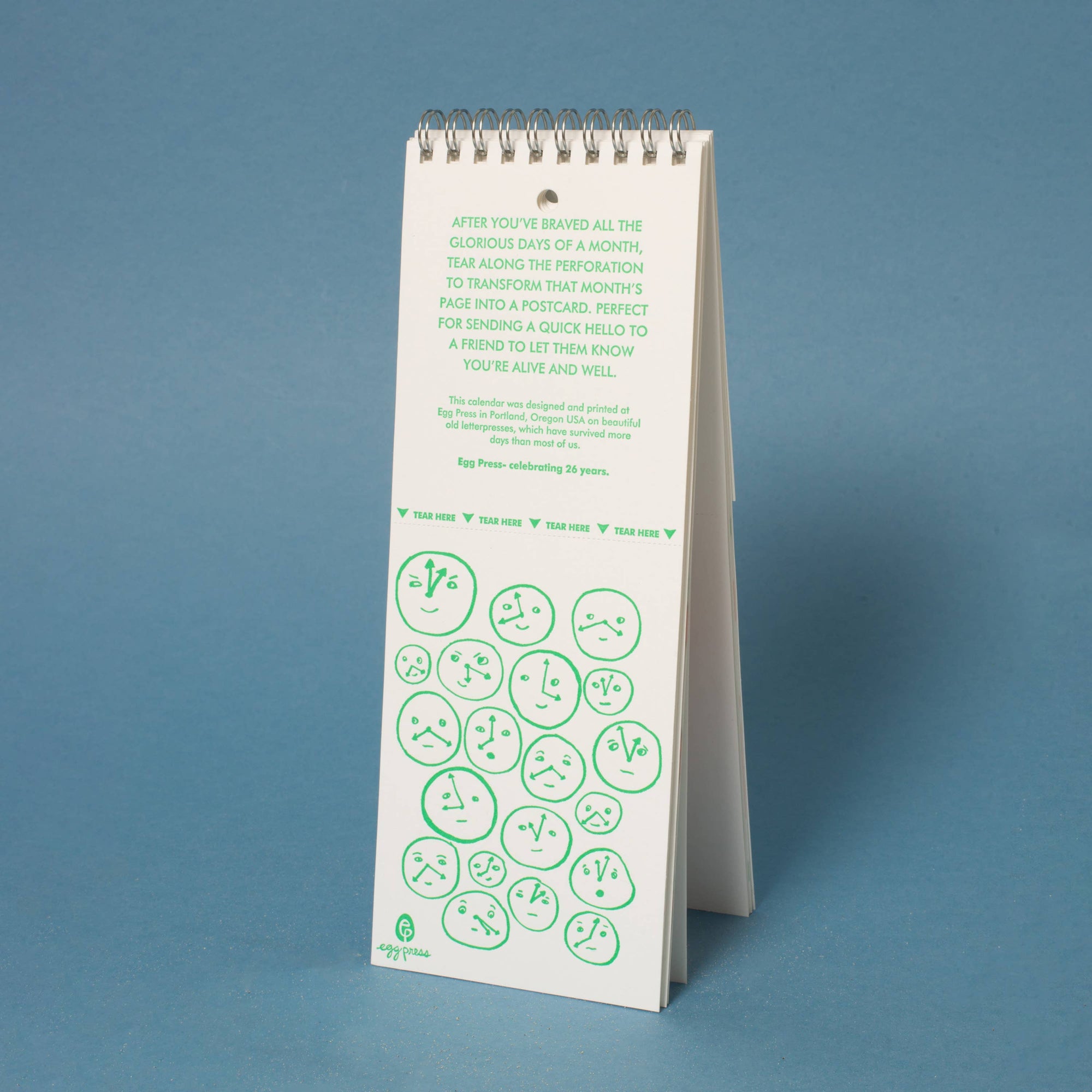 White spiral-bound calendar with green text and designs on a blue background