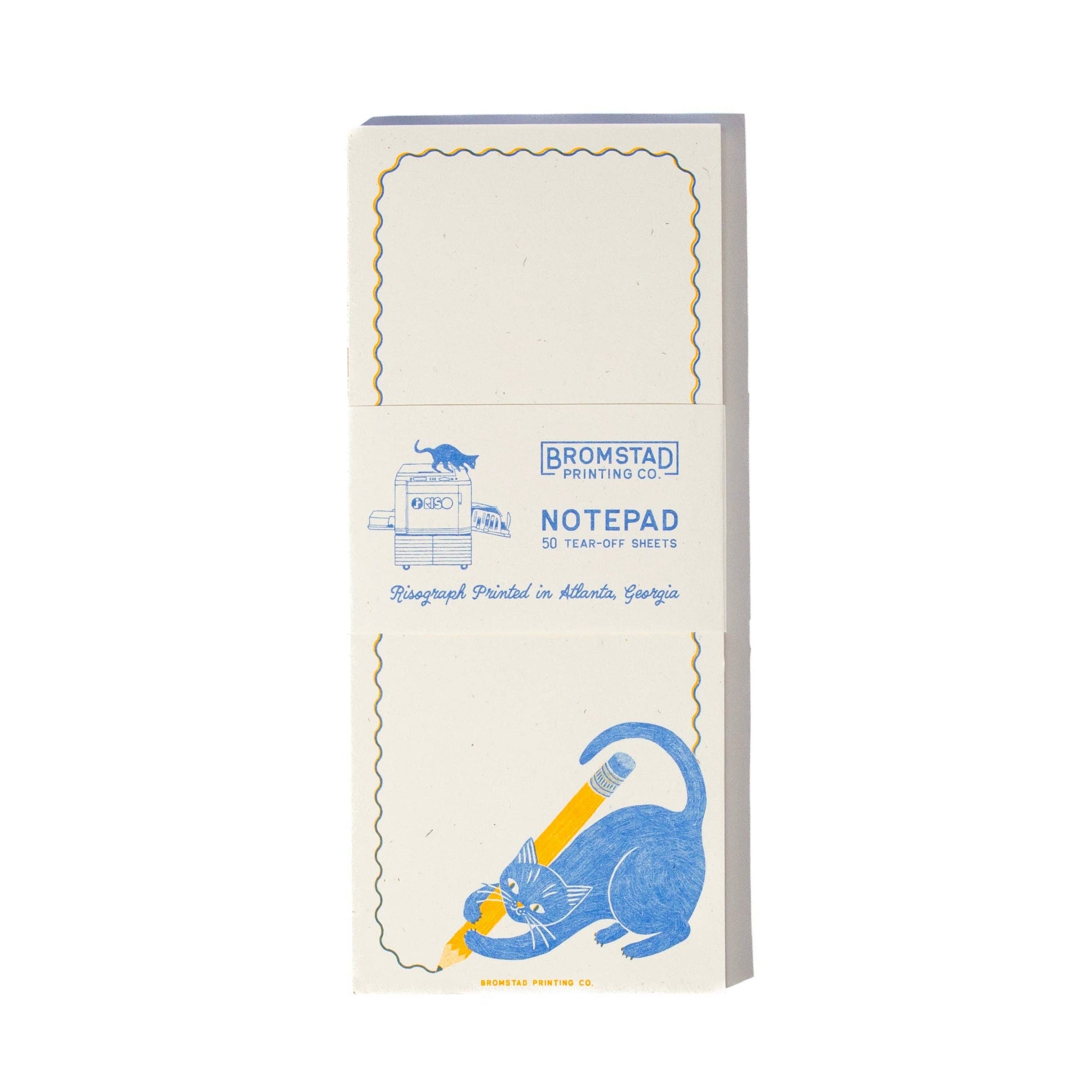 A cream-colored notepad with blue and yellow printed graphics, wrapped in a paper band that reads 'BROMSTAD PRINTING CO. NOTEPAD'.