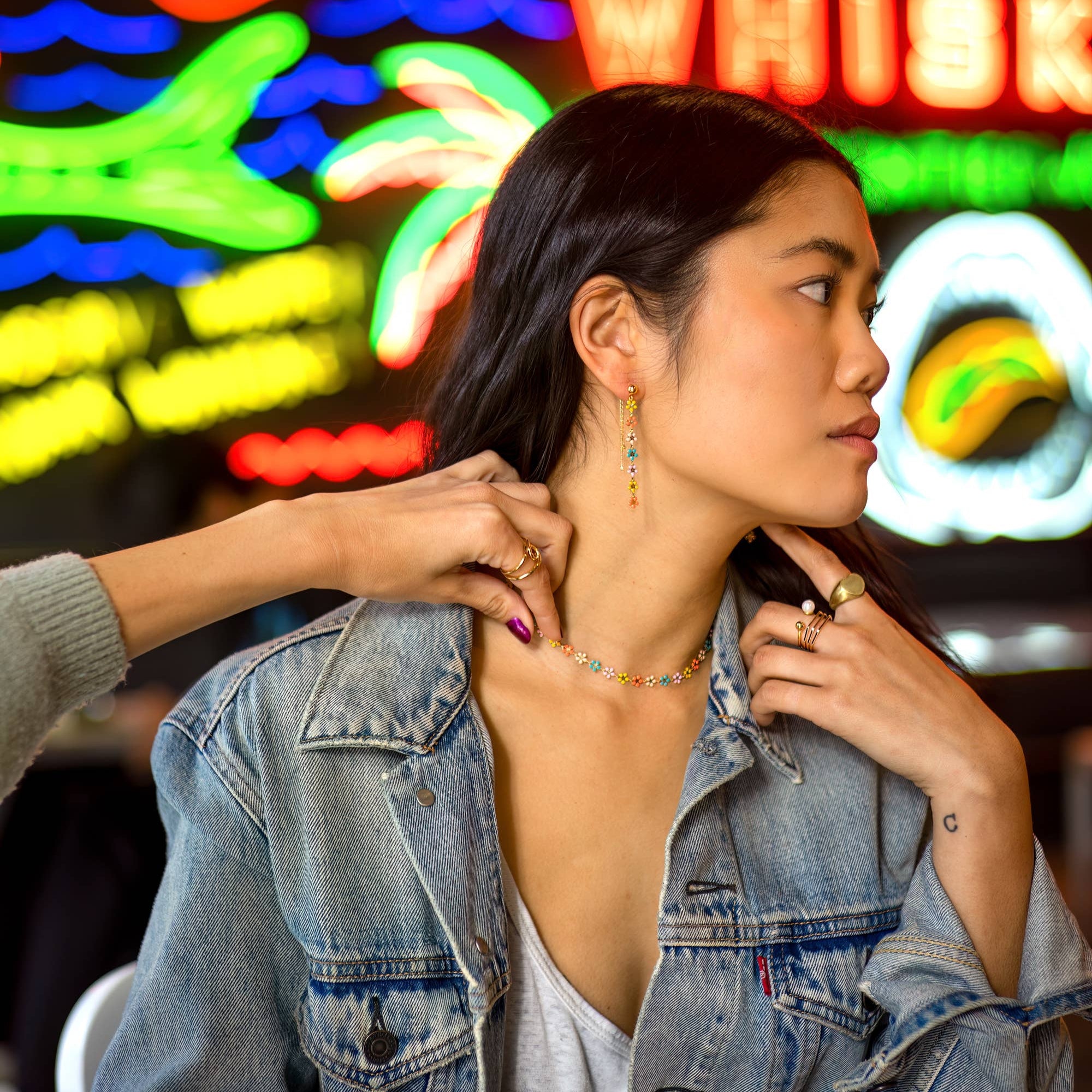 Woman adjusting necklace in front of colorful neon signs