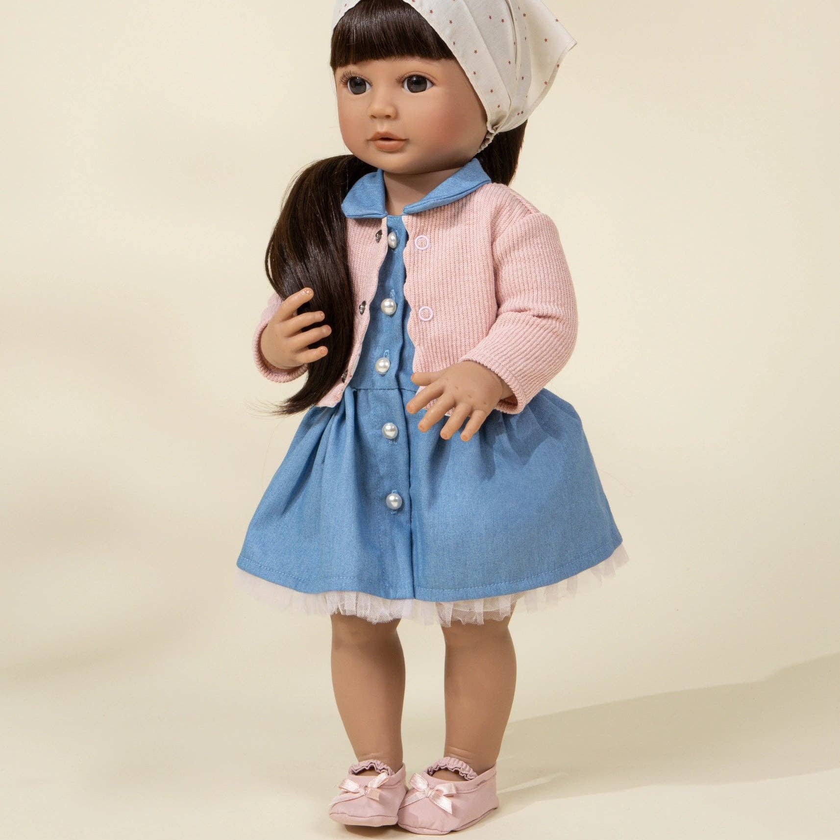 Doll wearing a pink sweater, blue dress, and white bonnet on a beige background