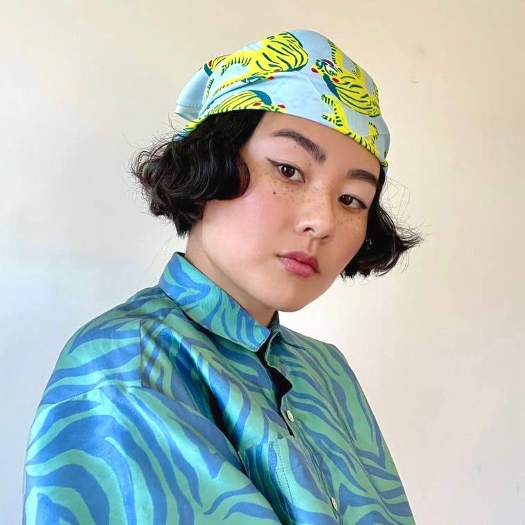 Person wearing a colorful headscarf and shirt with a plain background