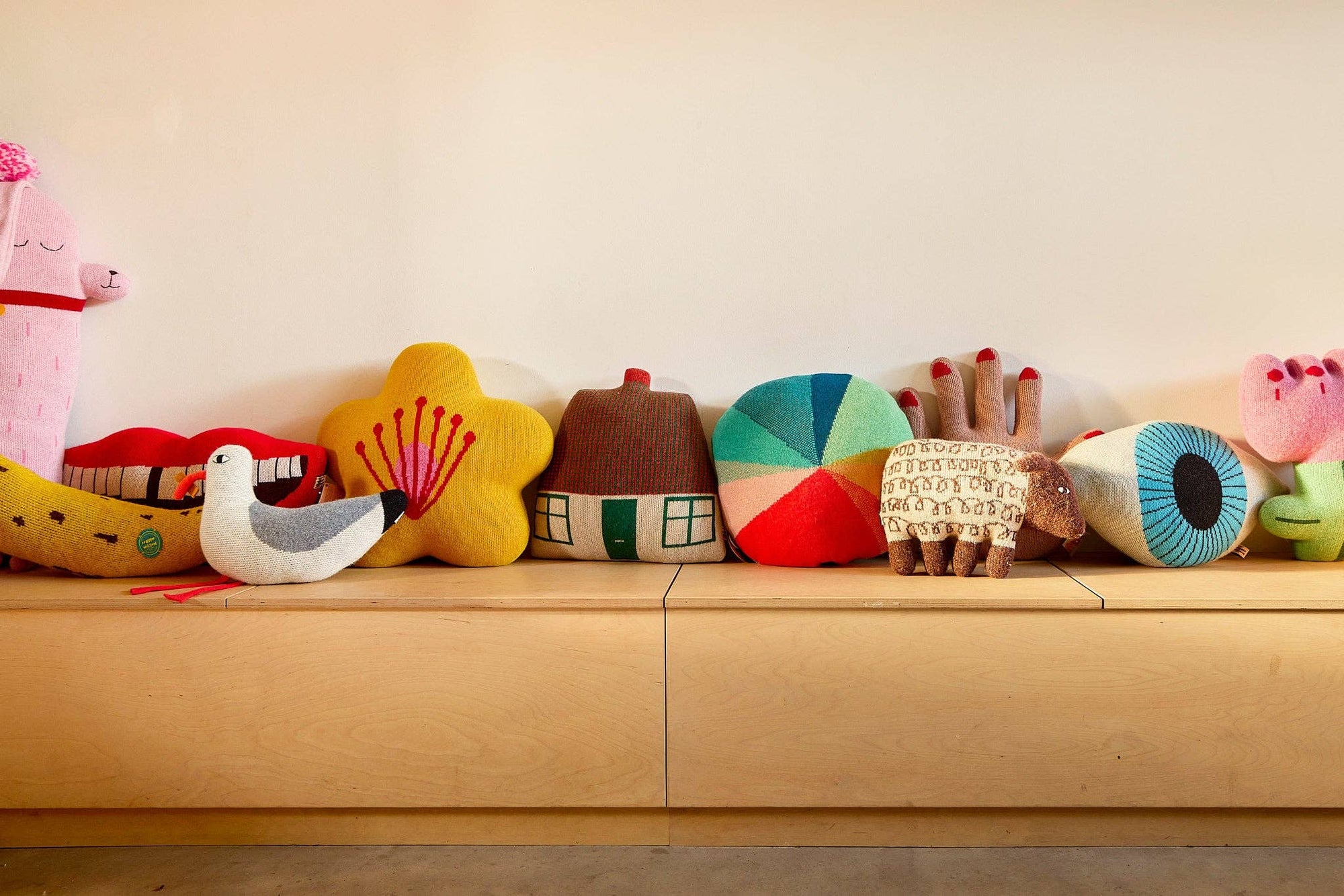 Row of colorful plush toys on a wooden shelf against a light background