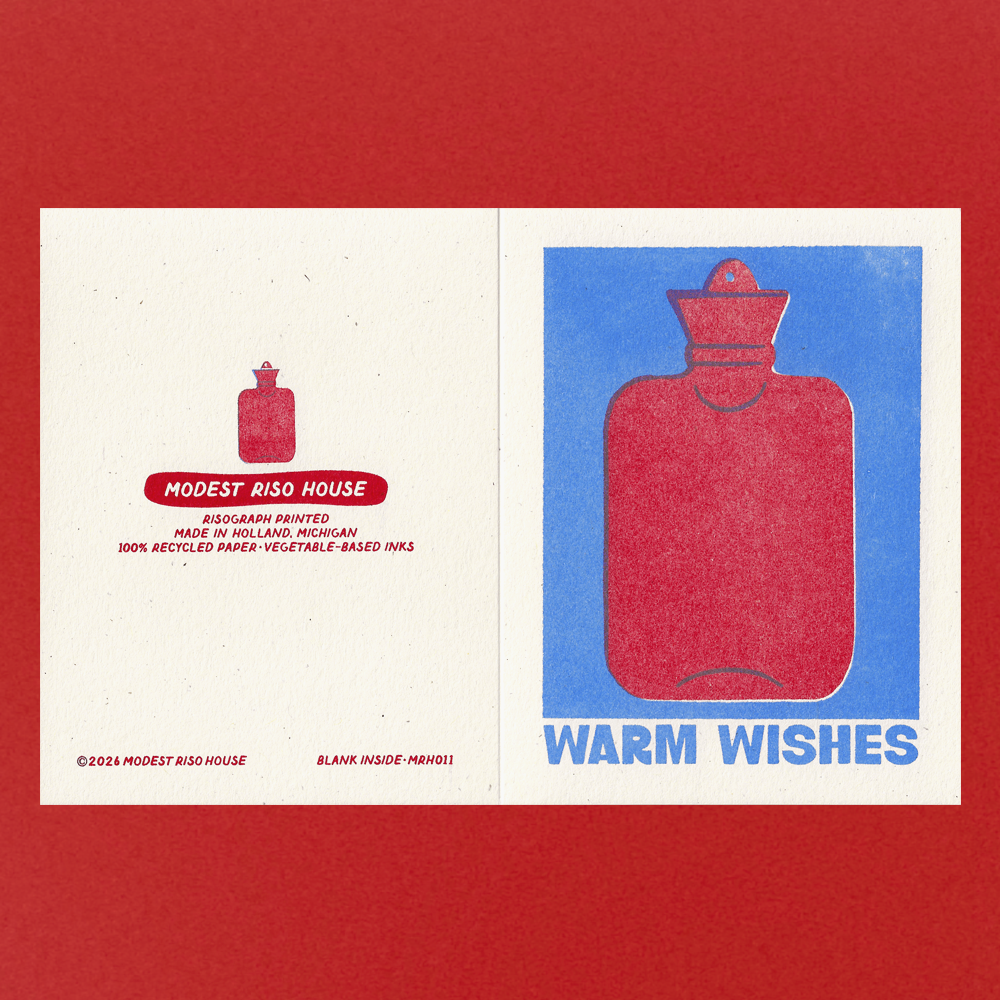 A flat lay of a Modest Riso House blank art print card, showing both the front and back designs. The card features a minimalist red hot water bottle illustration on a split cream and blue background, with the text 'WARM WISHES' on the front and product details on the back, all set against a solid red background.