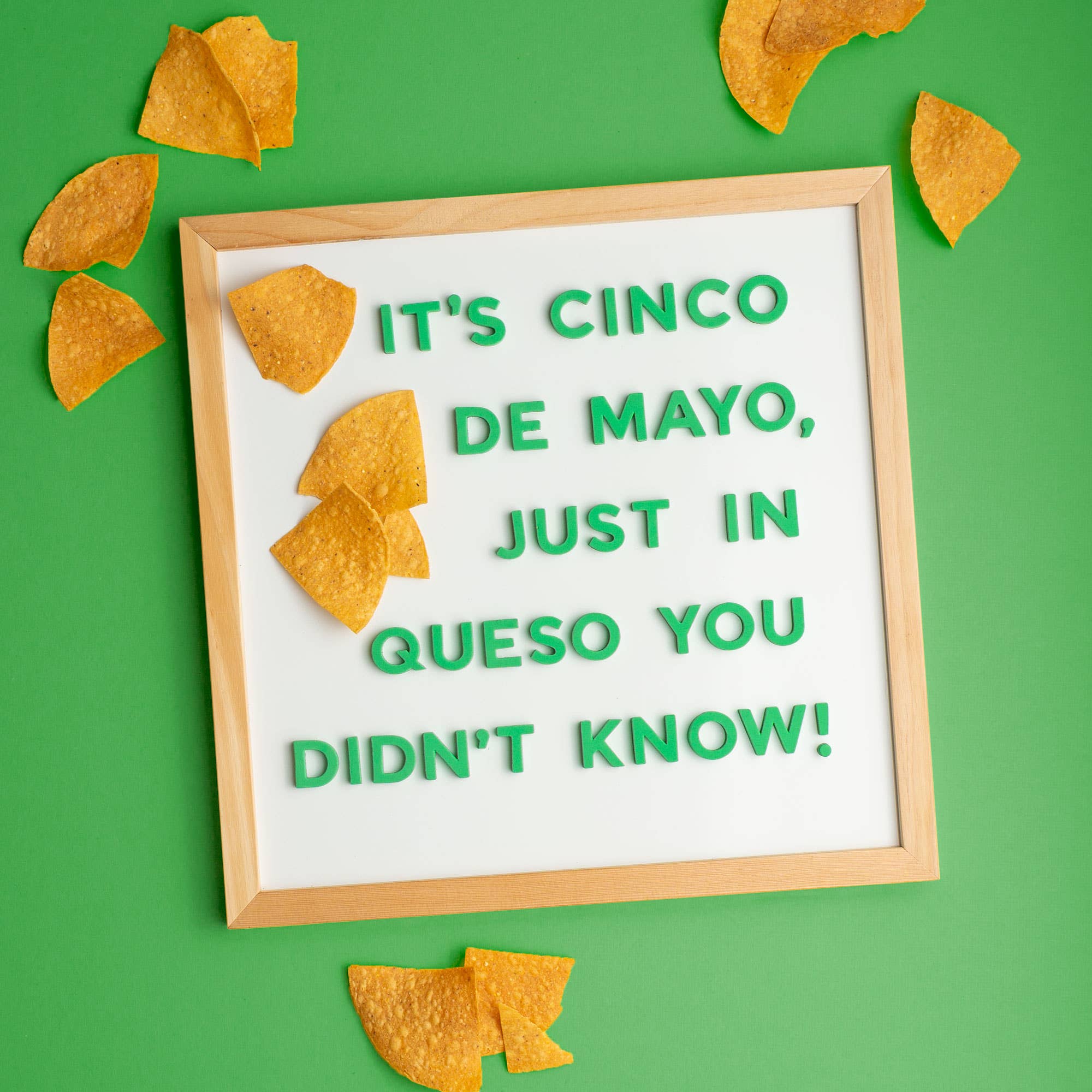 Framed sign with Cinco de Mayo message surrounded by tortilla chips on a green background