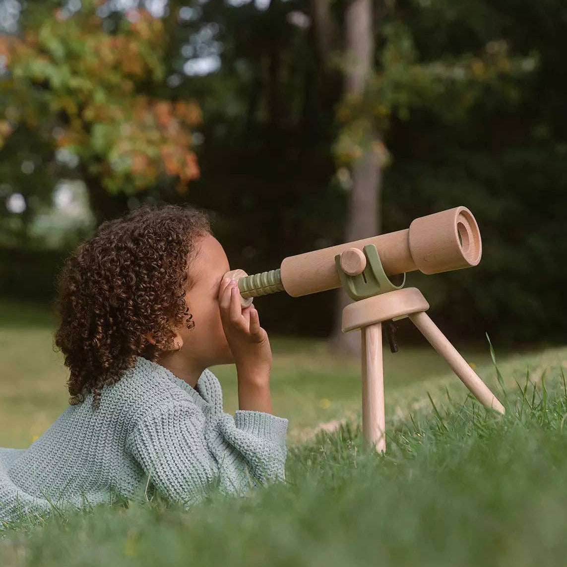 Child playing with a cardboard telescope in a grassy area with trees in the background