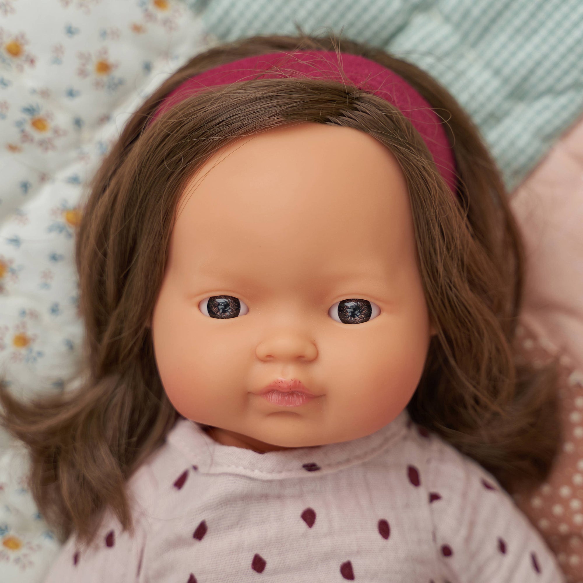Close-up of a doll with brown hair and a pink headband, wearing a polka dot outfit.