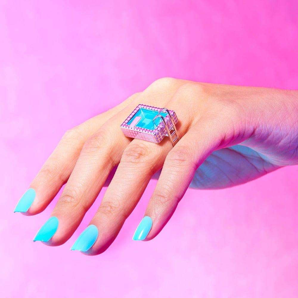 Hand wearing a colorful ring with turquoise nail polish on a pink background