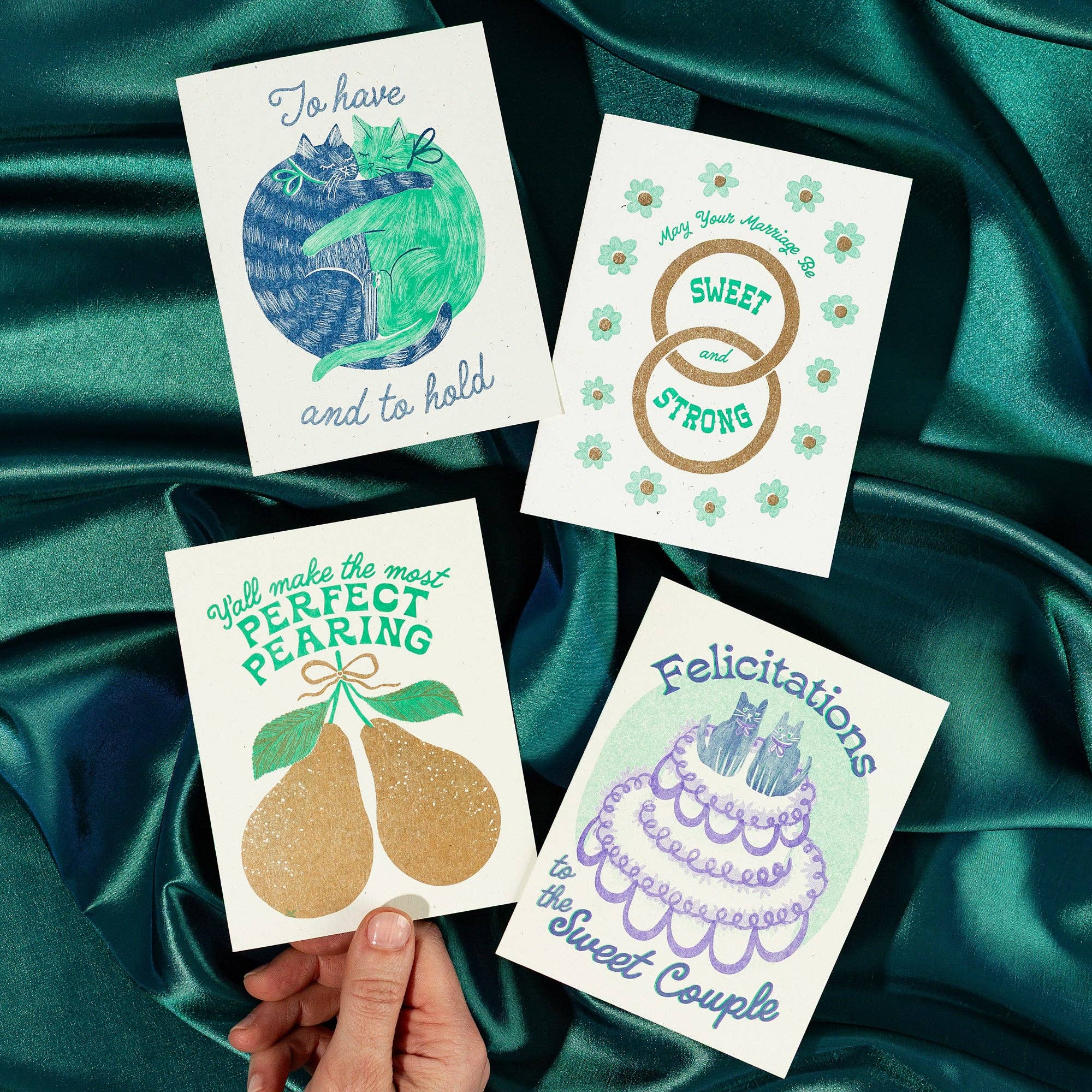 Four greeting cards with different designs on a green satin background