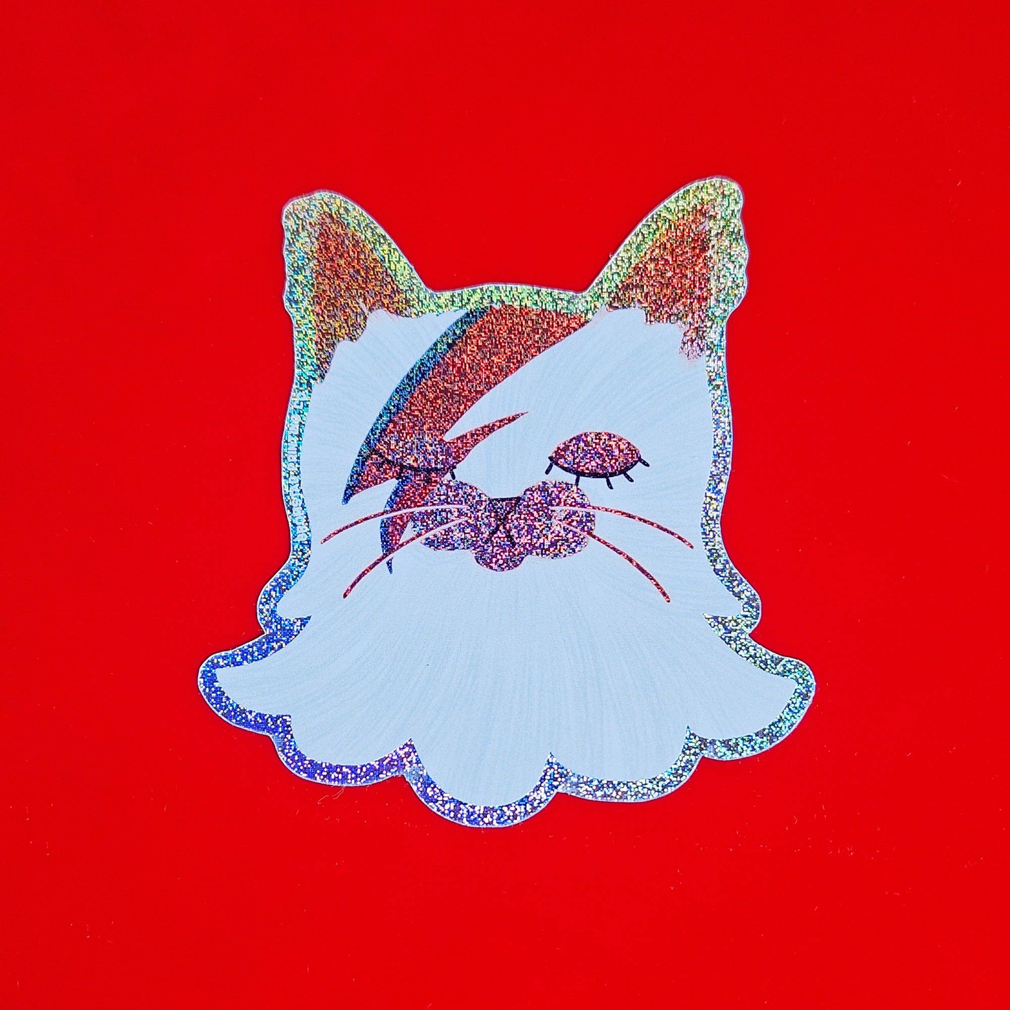 Decorative patch of a cat's face with glittery accents on a red background