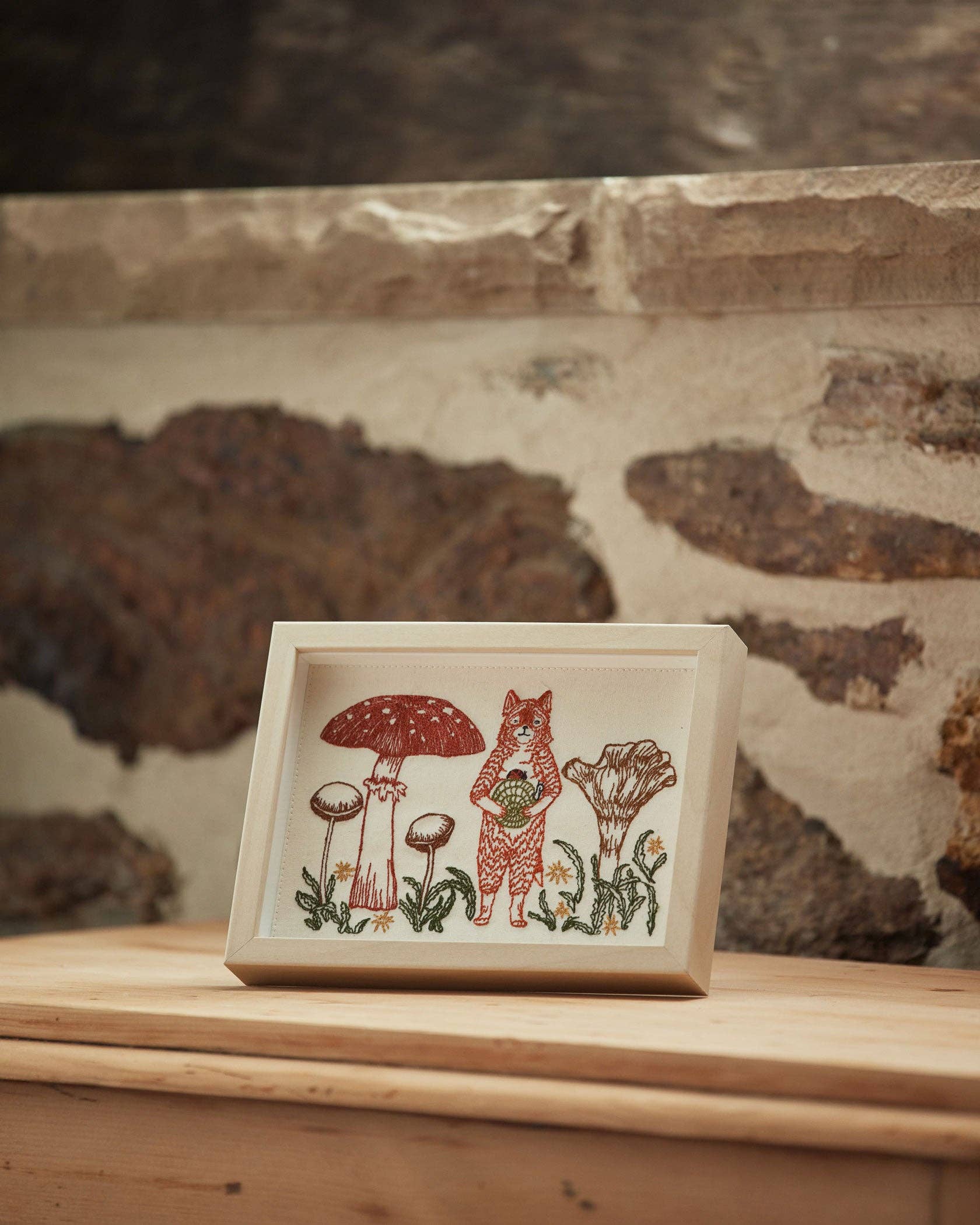 Framed artwork with a fox and mushroom design on a wooden surface.