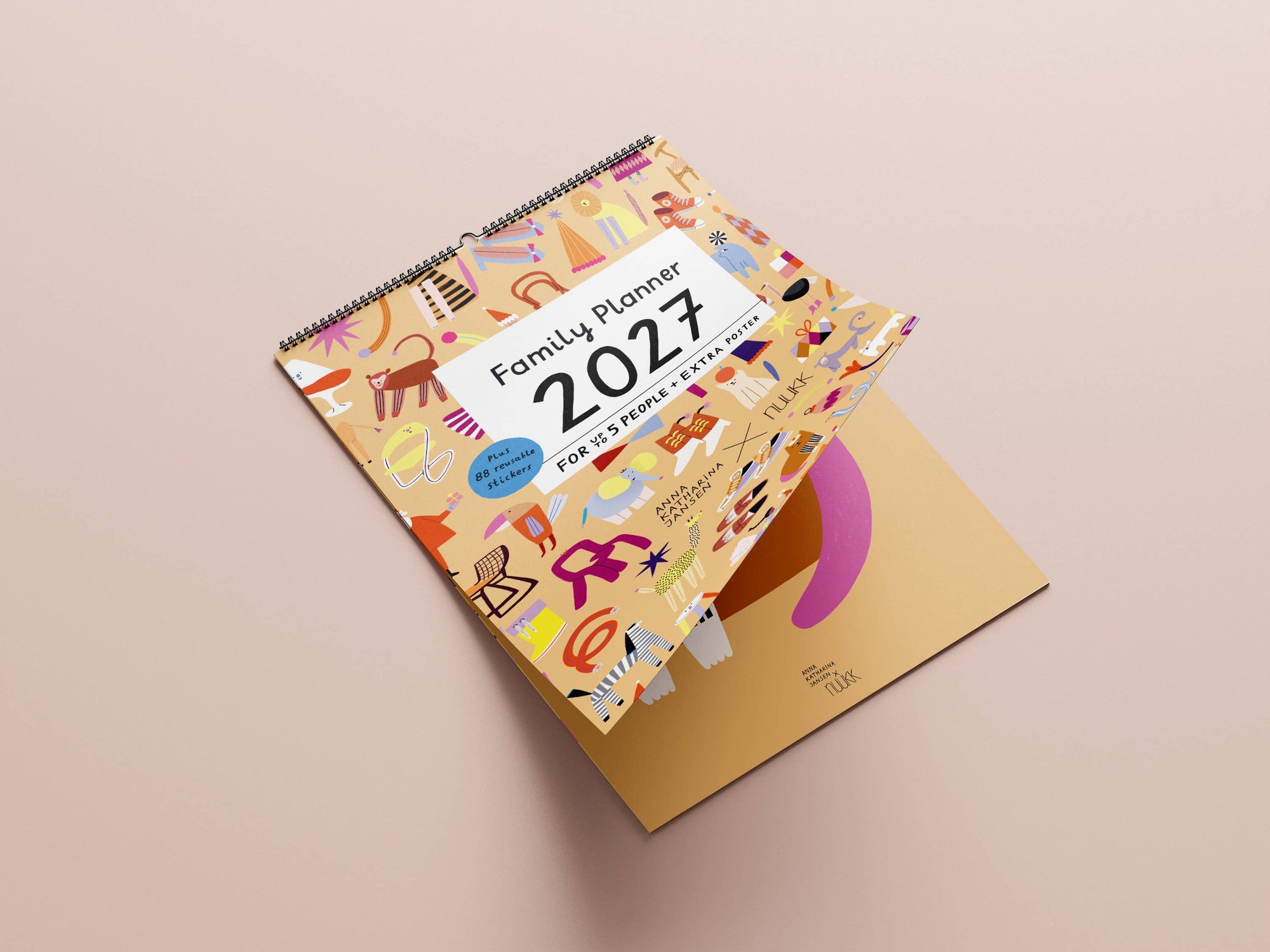A 2027 spiral-bound family planner with a colorful illustrated cover, shown open to reveal a gold interior page on a soft beige background.
