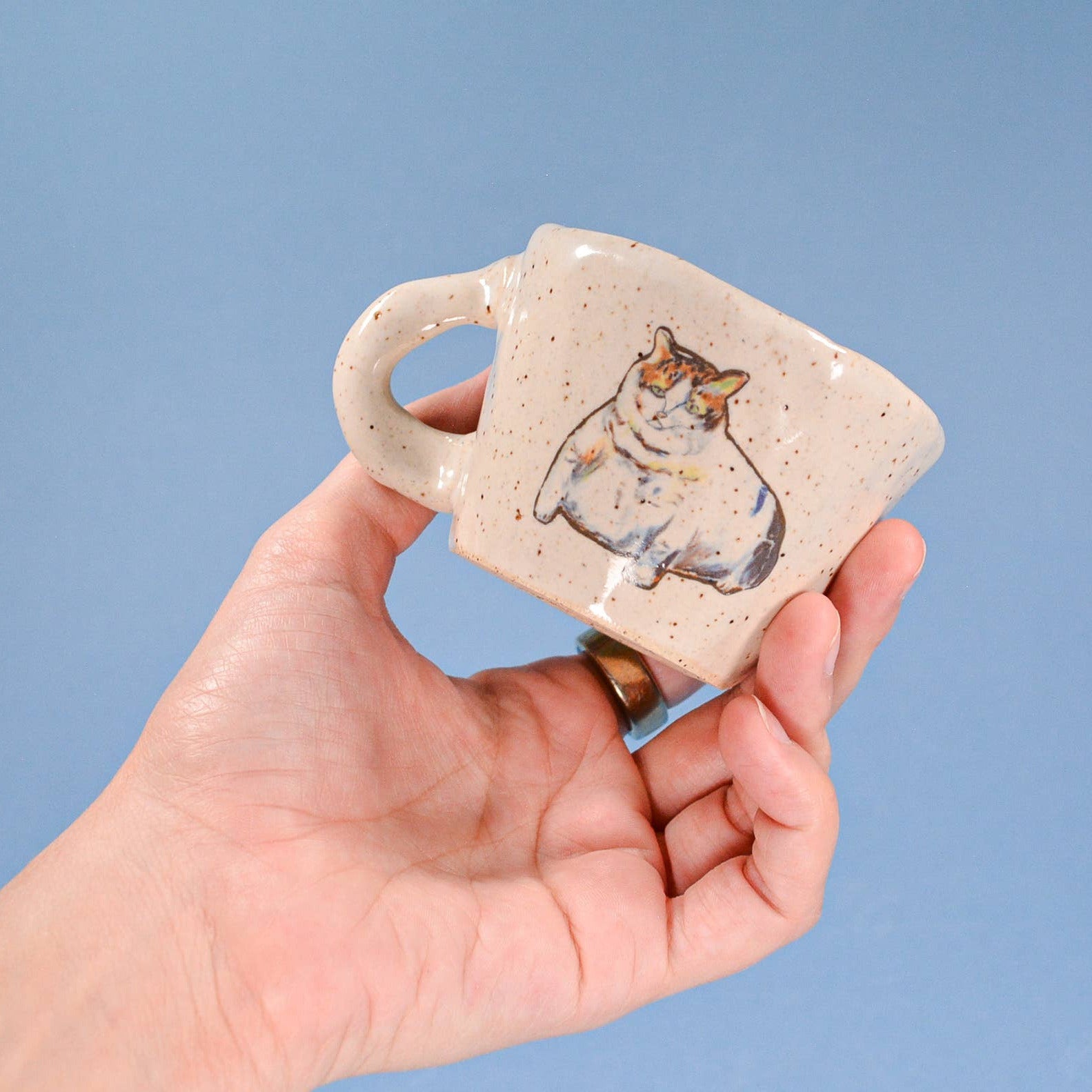 Hand holding a small ceramic mug with a dog design against a blue background