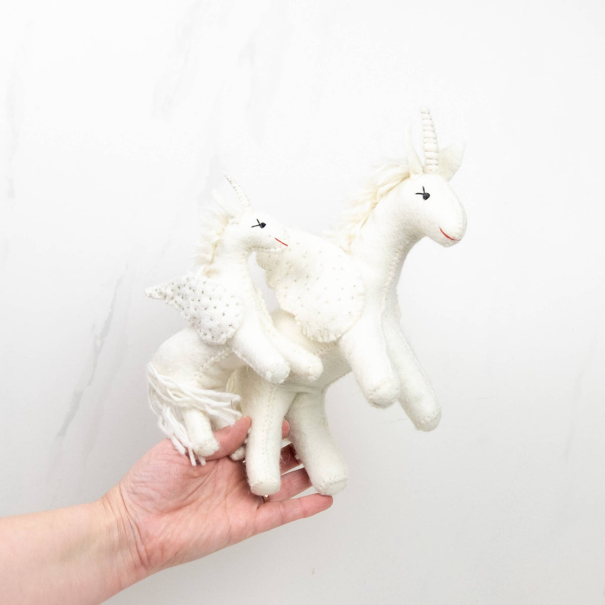 White plush unicorn toy held in a hand against a light background