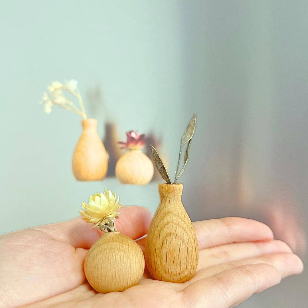 Two small wooden vases with decorative elements held in a hand against a blurred background.