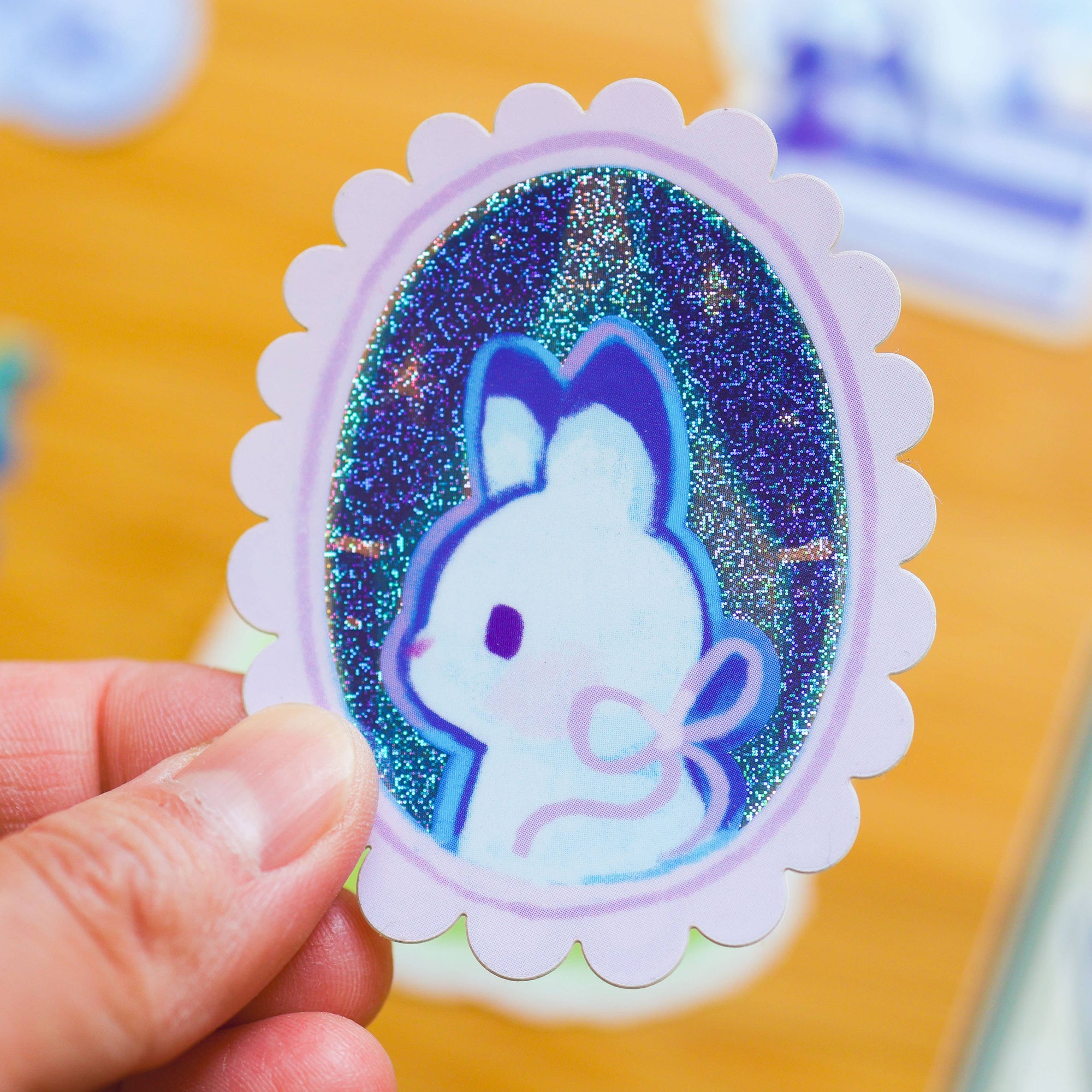 Hand holding a glittery sticker with a cartoon character on a blurred background