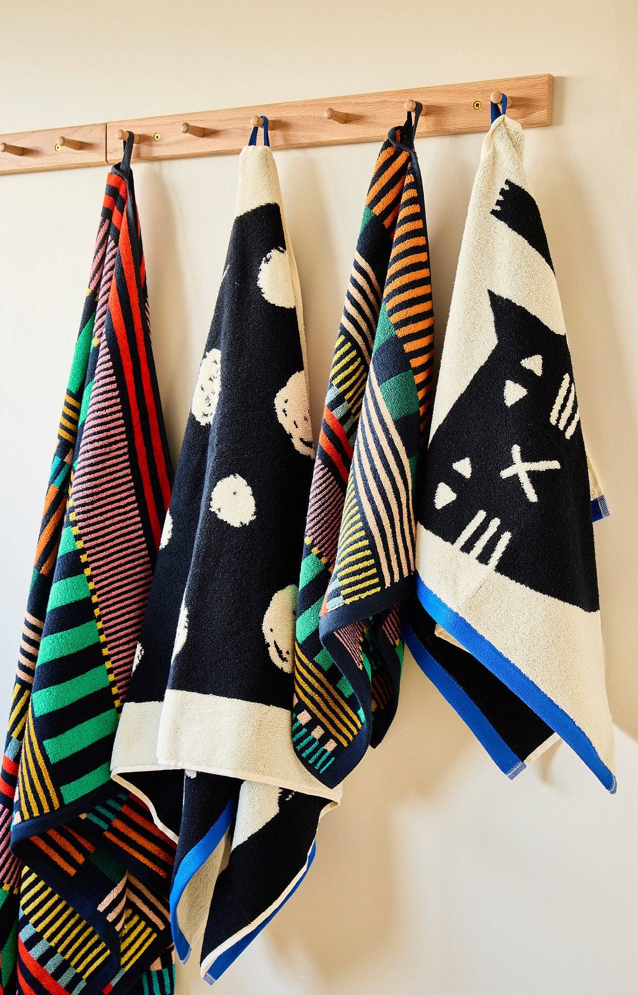 Colorful patterned towels hanging on a wooden rack against a white wall.