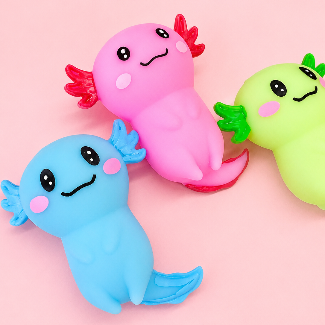 Three cute, cartoonish axolotl-shaped squishy toys in blue, pink, and green, arranged on a solid light pink background.