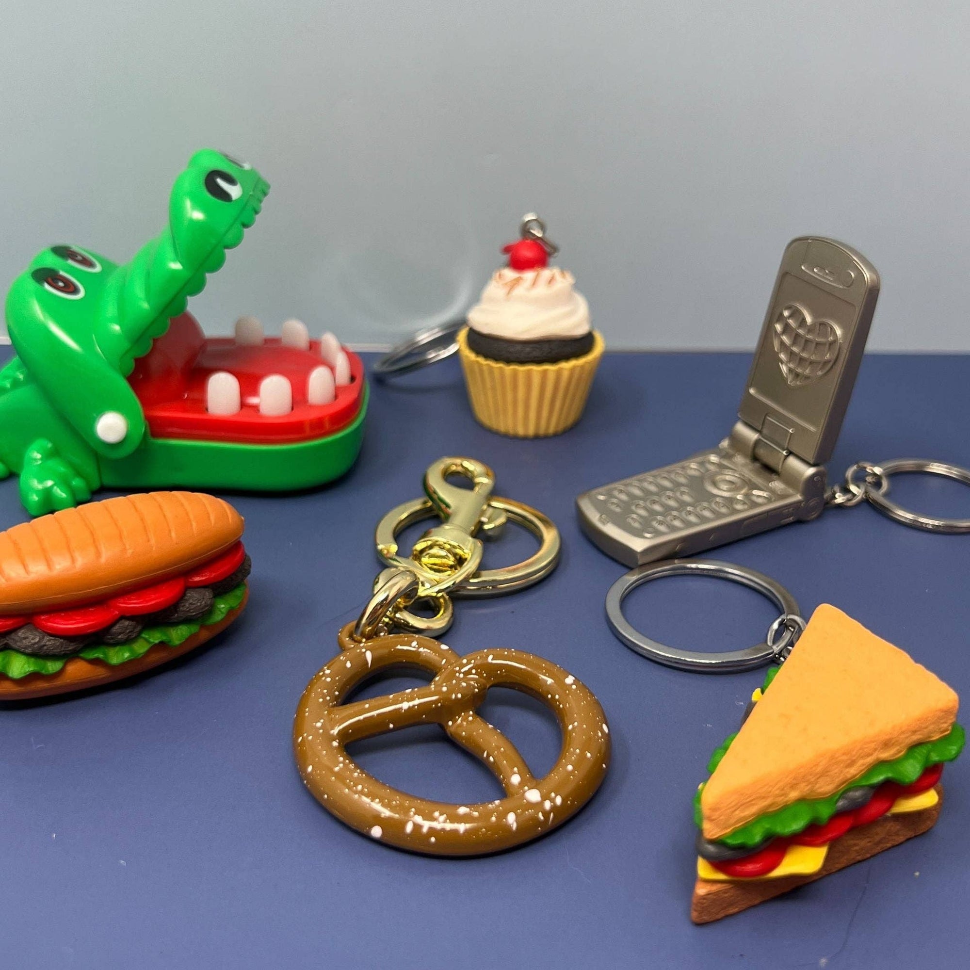 Collection of novelty keychains including a pretzel, hamburger, and phone on a blue surface.