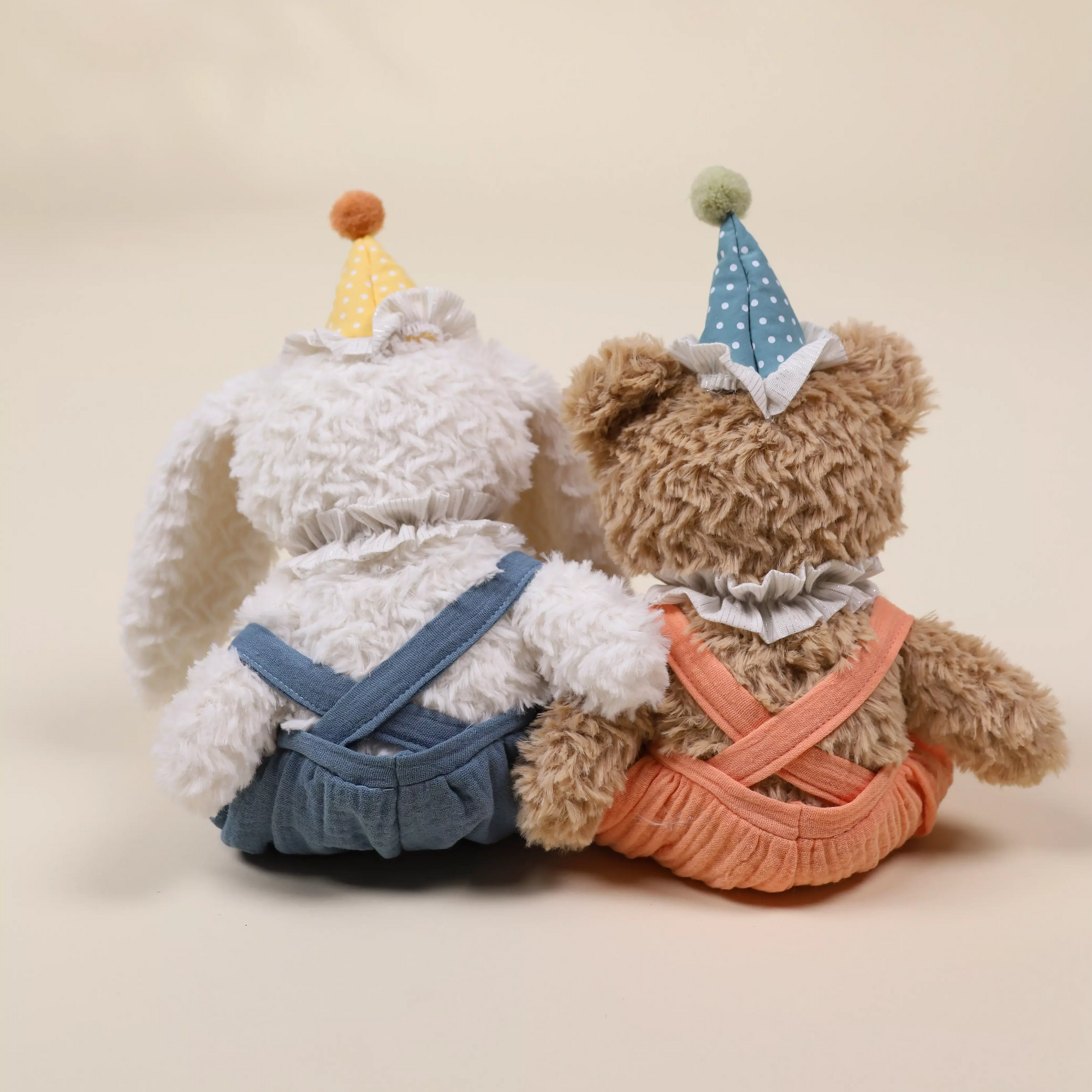 Two teddy bears wearing party hats on a beige background