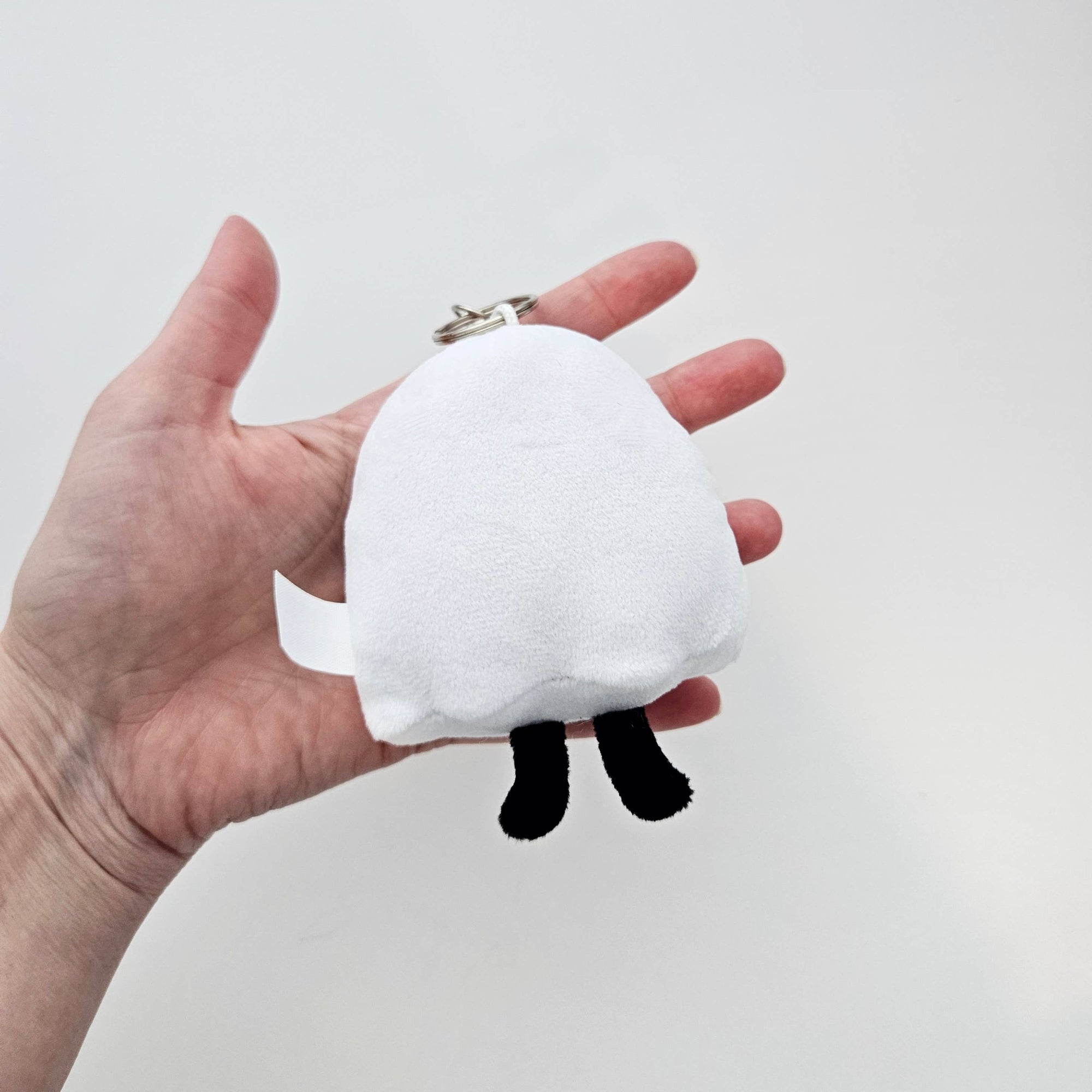 White plush keychain with black accents held in a hand against a light gray background