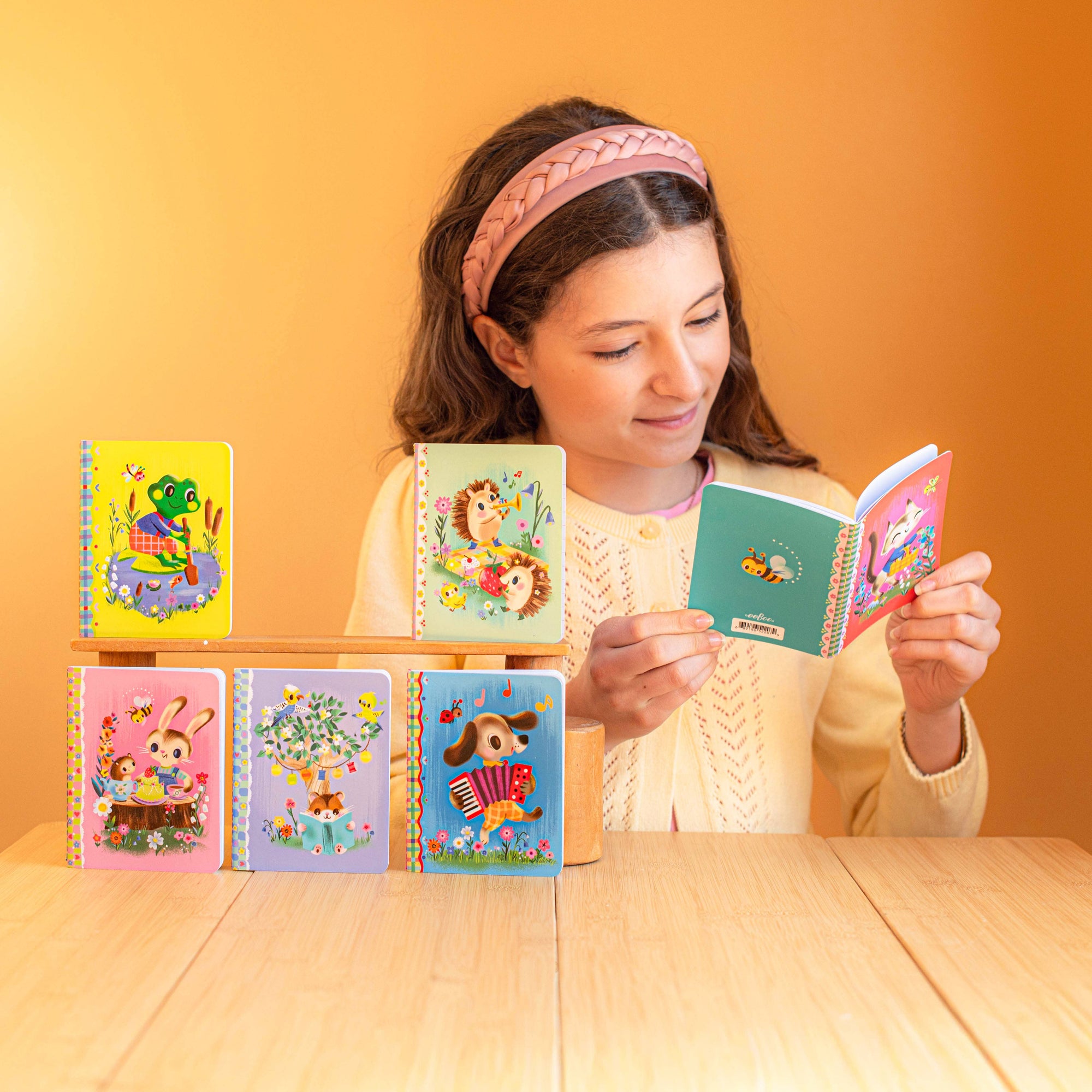 Girl holding a colorful book with other books on a wooden stand against an orange background