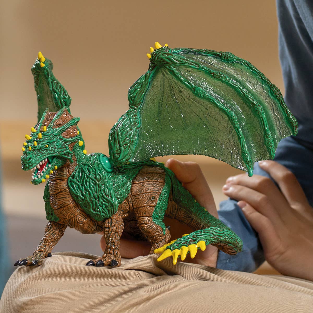 Green dragon toy figure held by a person on a beige surface