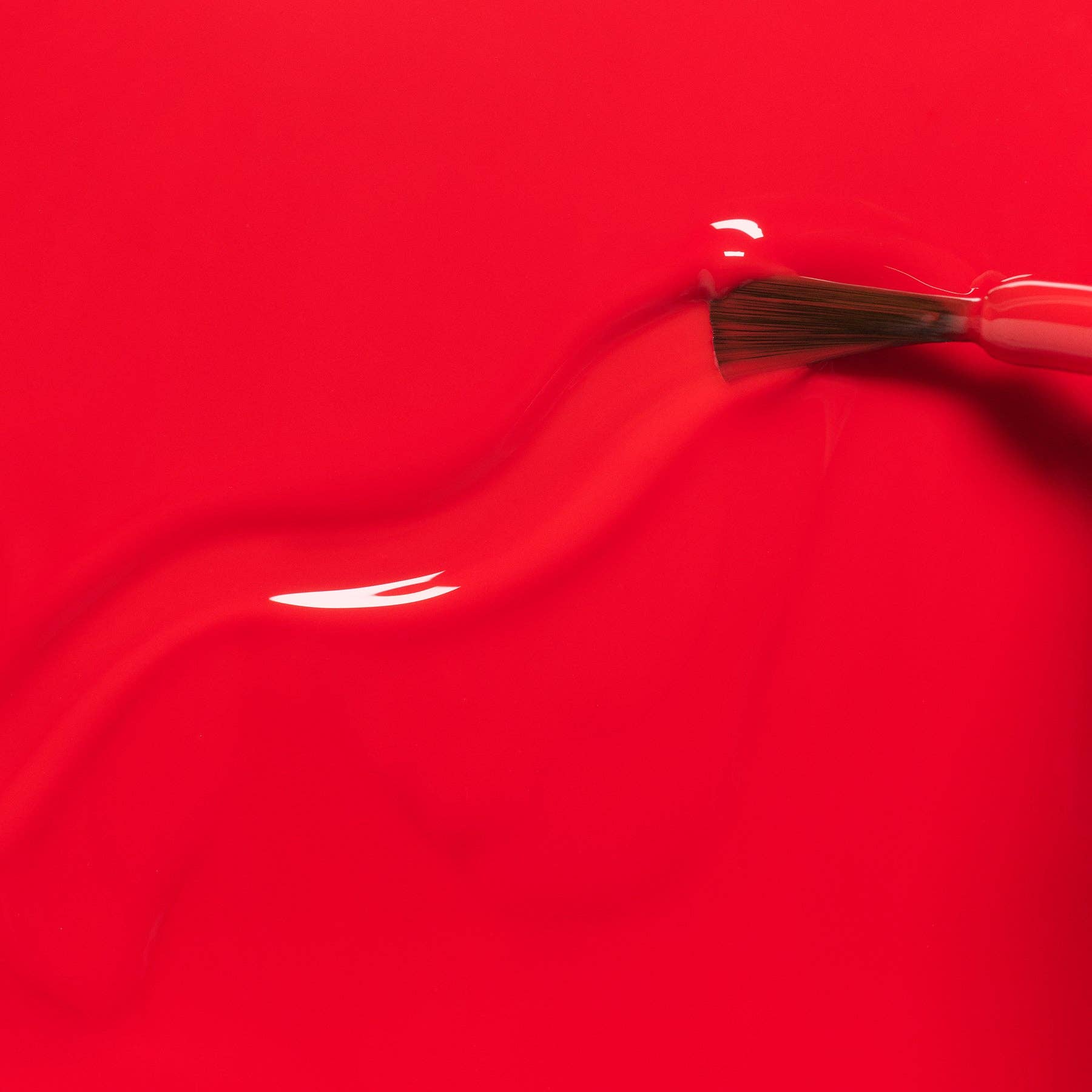 A close-up of a bright red glossy surface with a paintbrush applying or smoothing the red material.