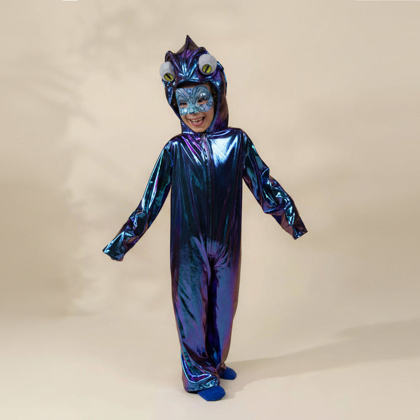 A child wearing a shiny holographic blue and purple one-piece costume with a hood featuring large cartoon eyes and a smiling face cutout, standing against a plain beige studio background.