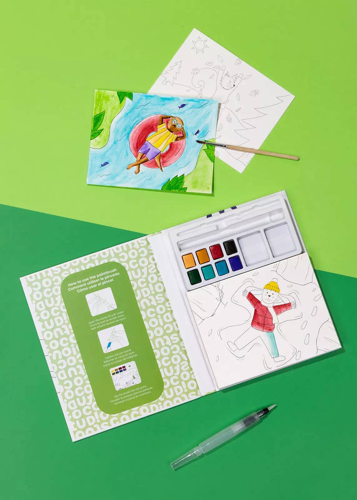 Artistic watercolor set with paint, brush, and coloring book on a green background