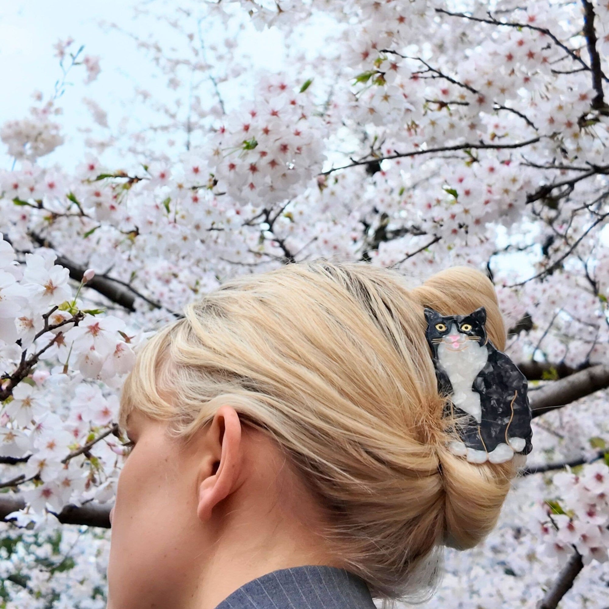 Person with a cat figurine in their hair against a cherry blossom background