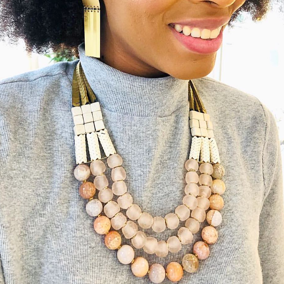 Woman wearing a beaded necklace and earrings, smiling outdoors.