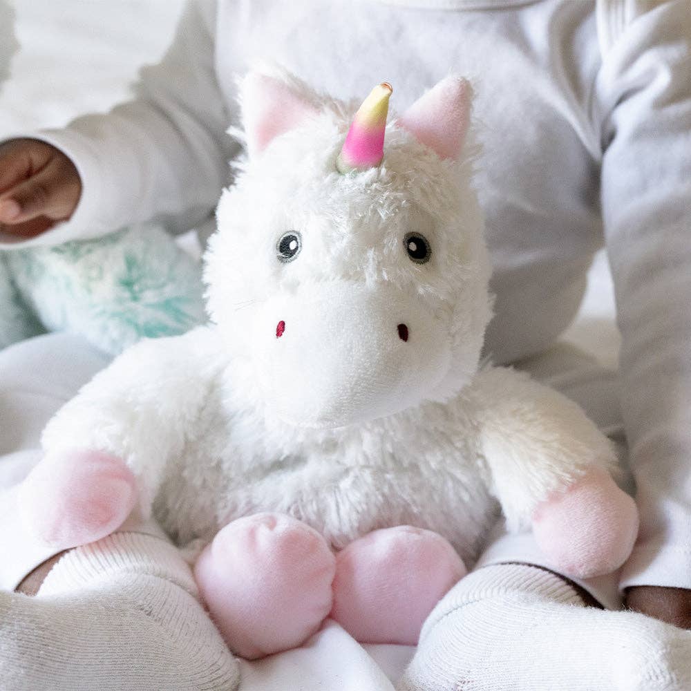 White plush unicorn toy held by a child wearing a white outfit.