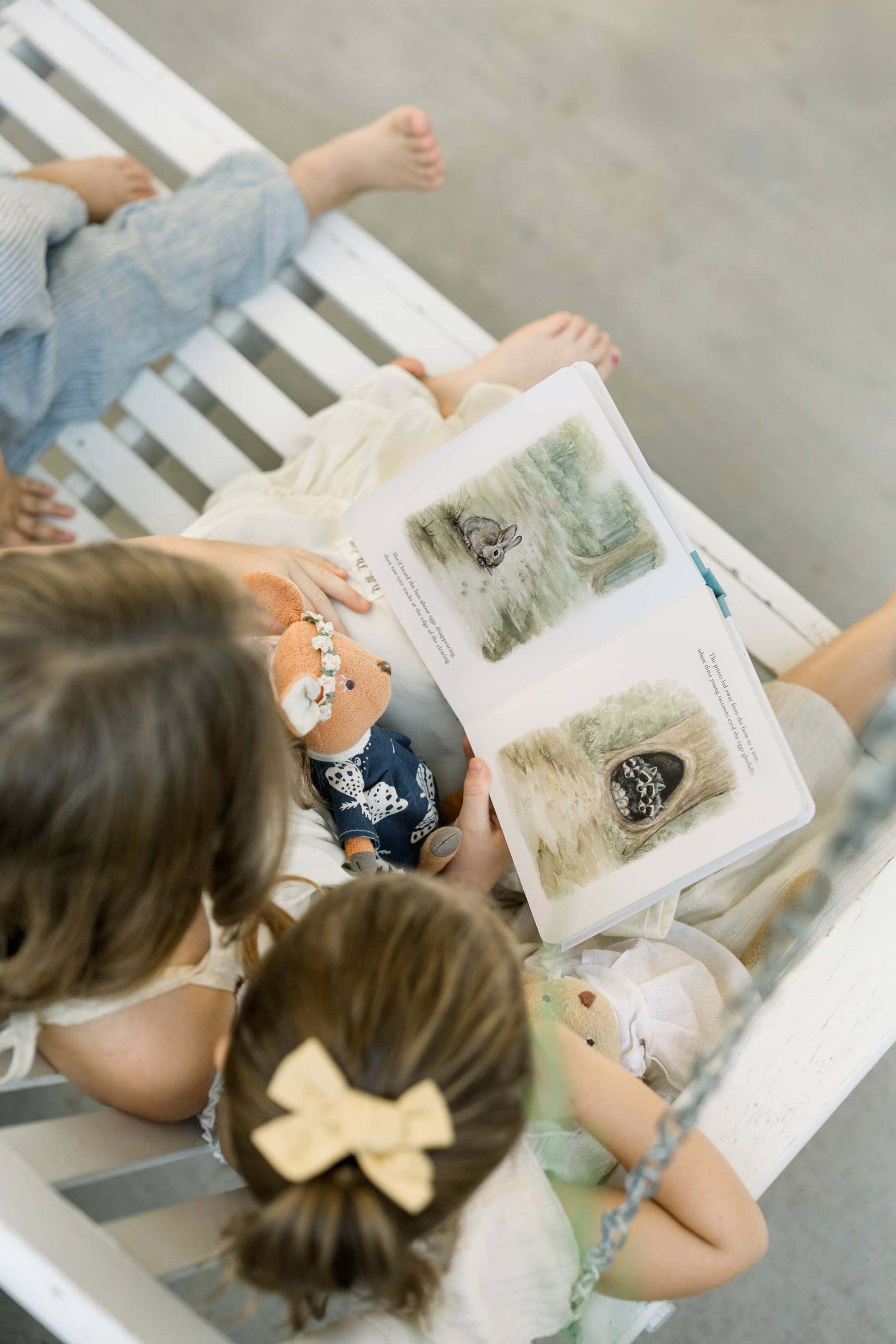Two children sitting on a white bench with a book open in front of them, showing illustrations.