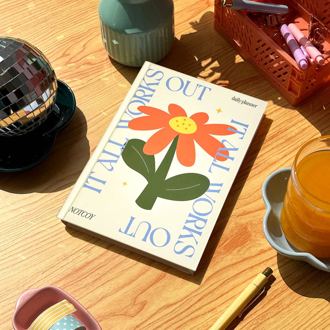 Planner with a floral design on a wooden table with a cup of tea and decorative items.