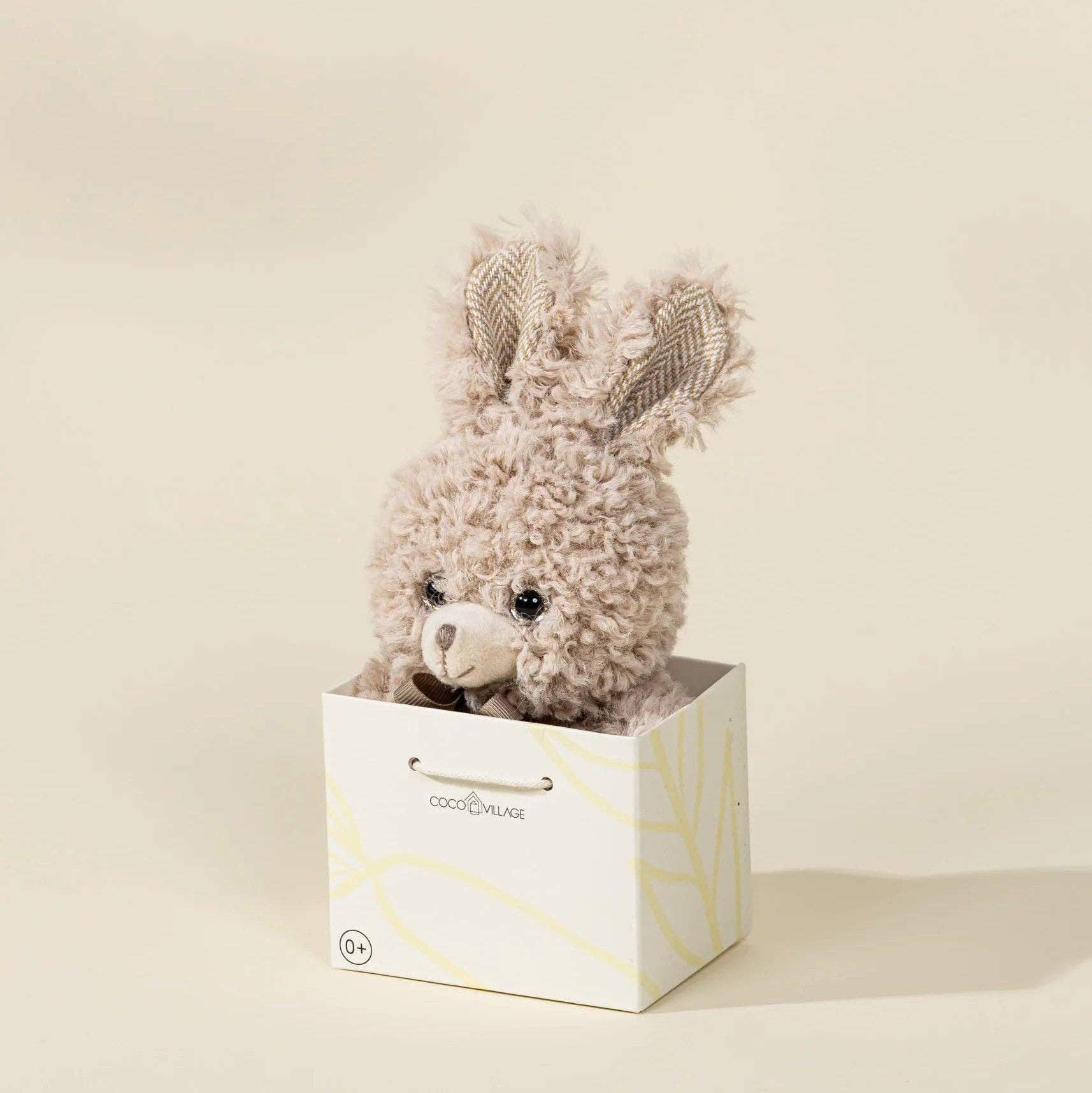Plush toy with bunny ears in a white box on a beige background