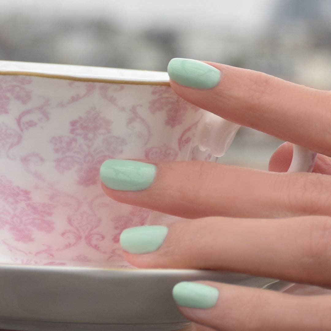 Hand with light green nail polish holding a patterned ceramic bowl.