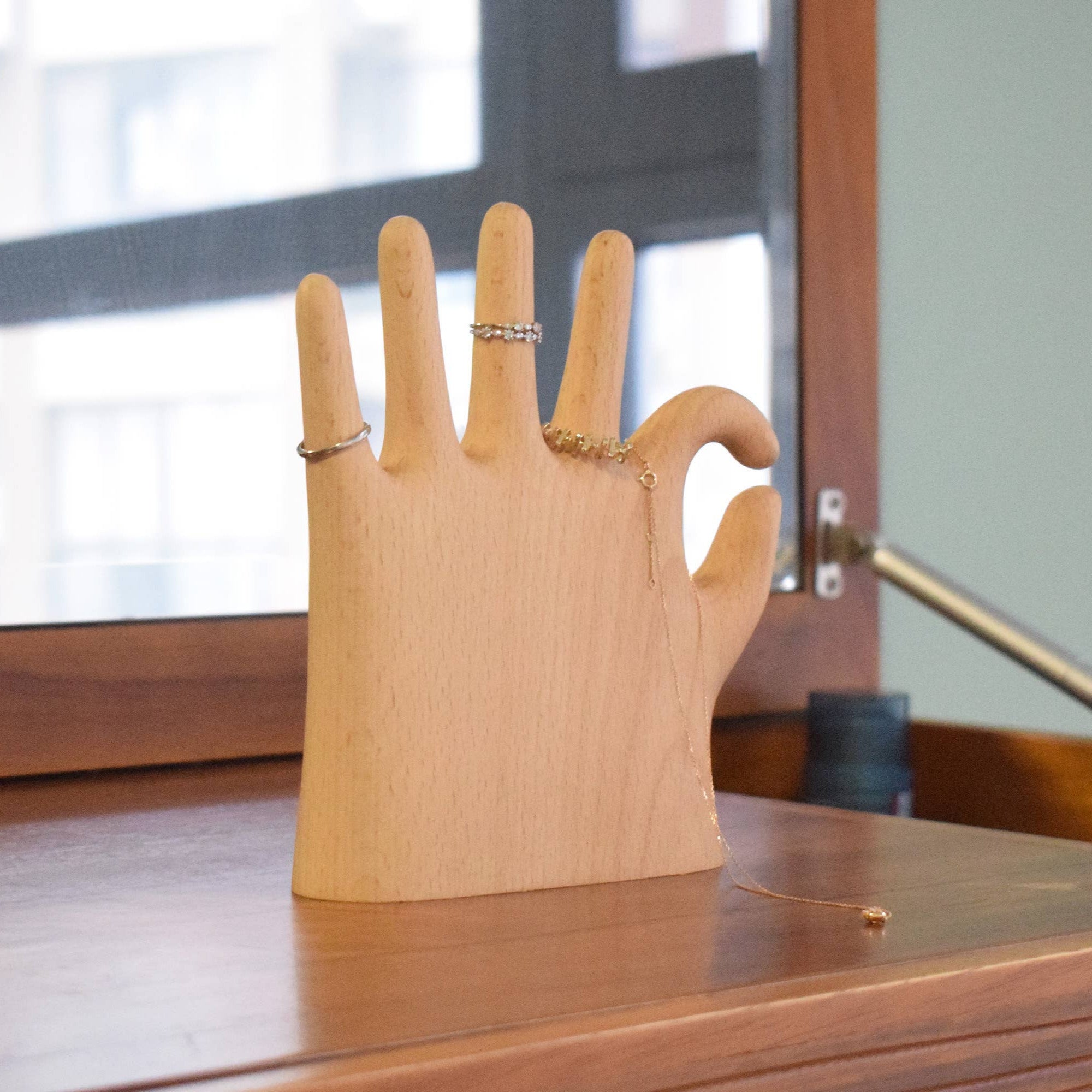 Wooden hand model with rings on a wooden surface, next to a bottle of Ambesssa product.