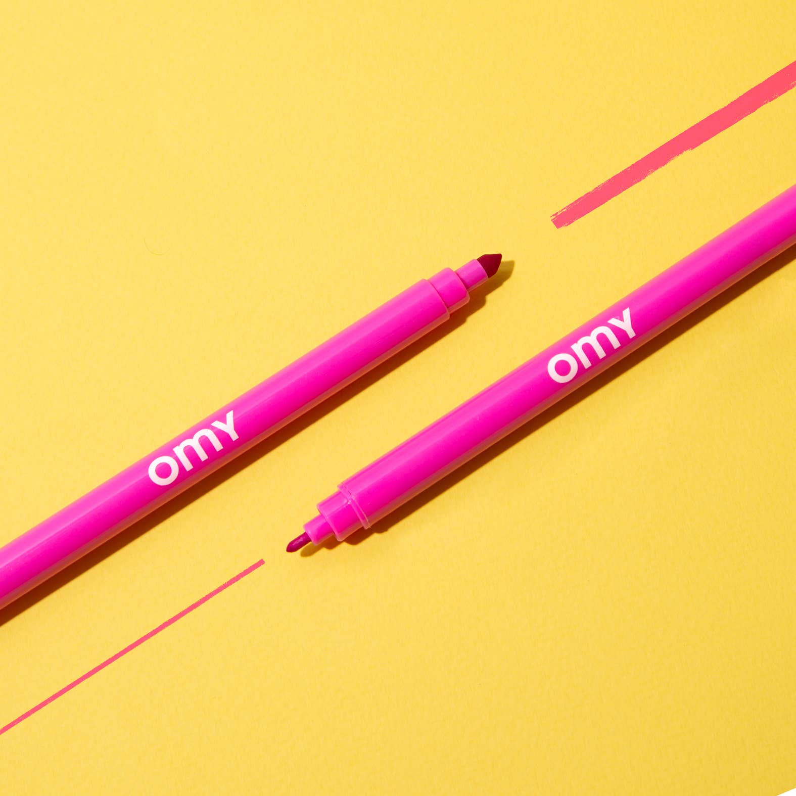 Two pink markers with 'omy' branding on a yellow background