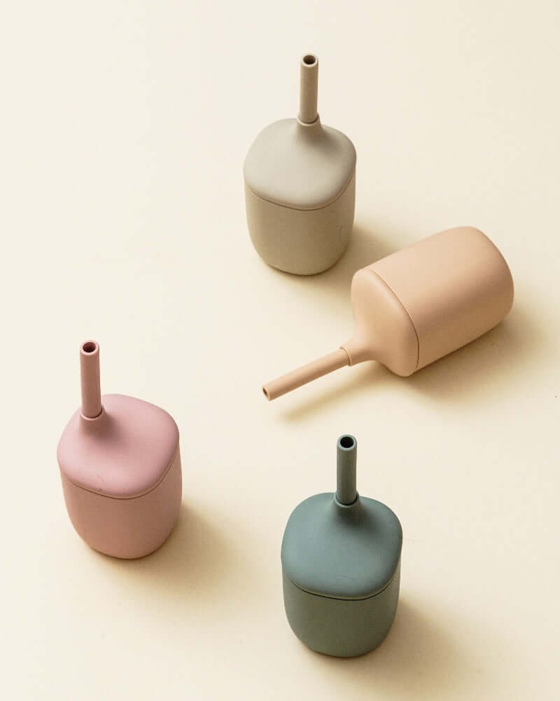 Set of four pastel-colored silicone containers with spouts on a beige background